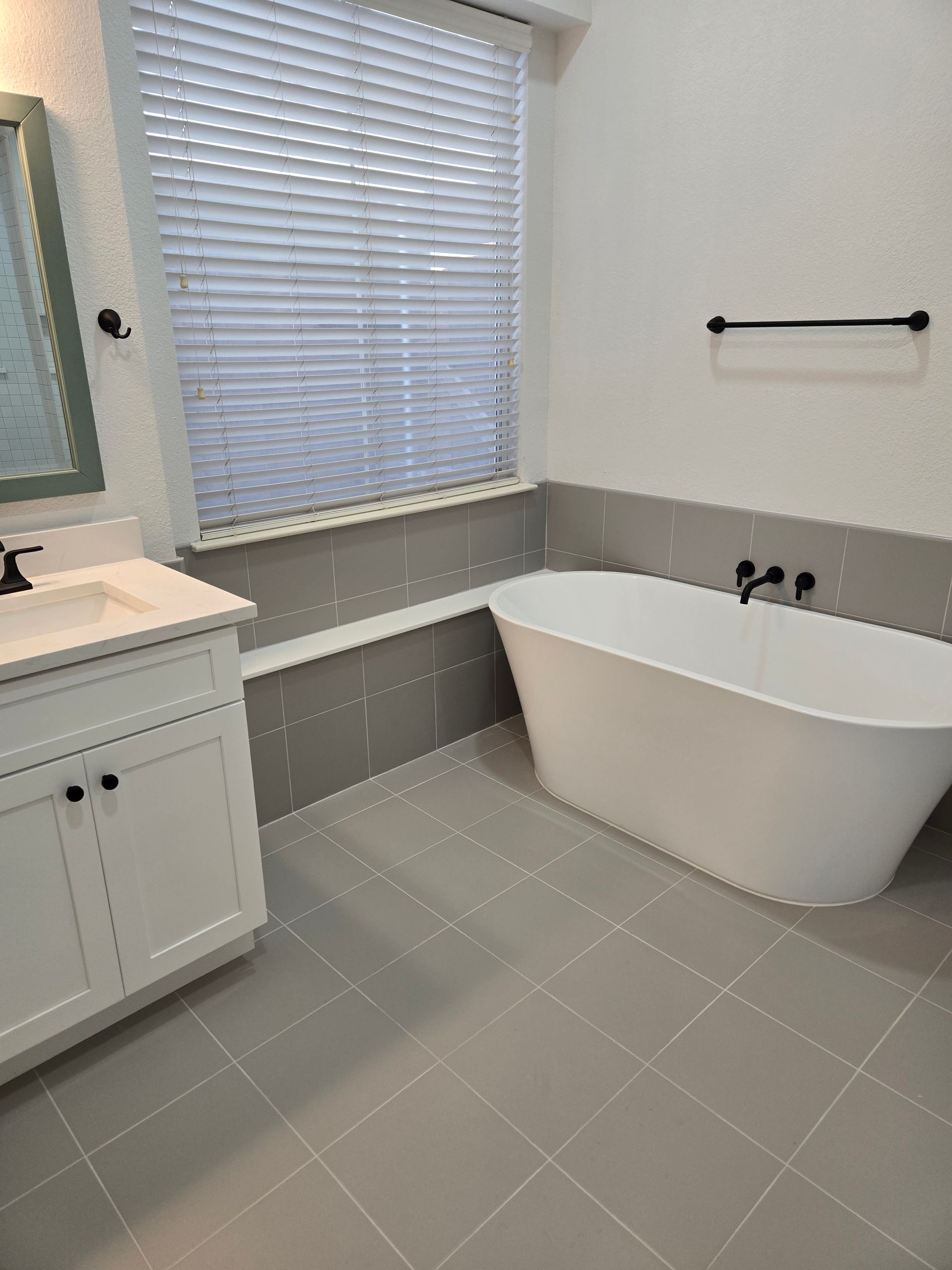 A bathroom with a bathtub , sink , mirror and window.