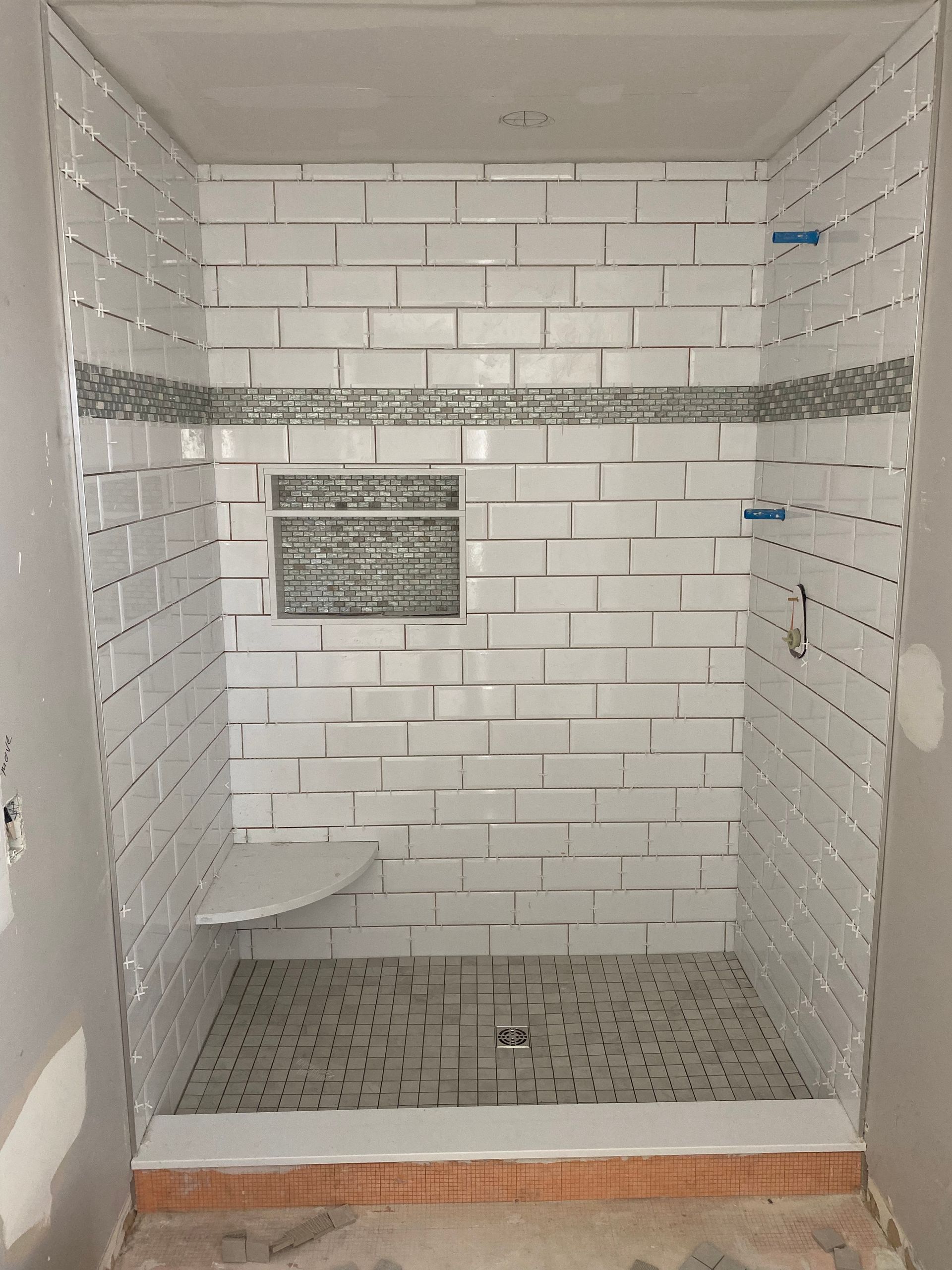 A shower stall with white tiles and a bench.