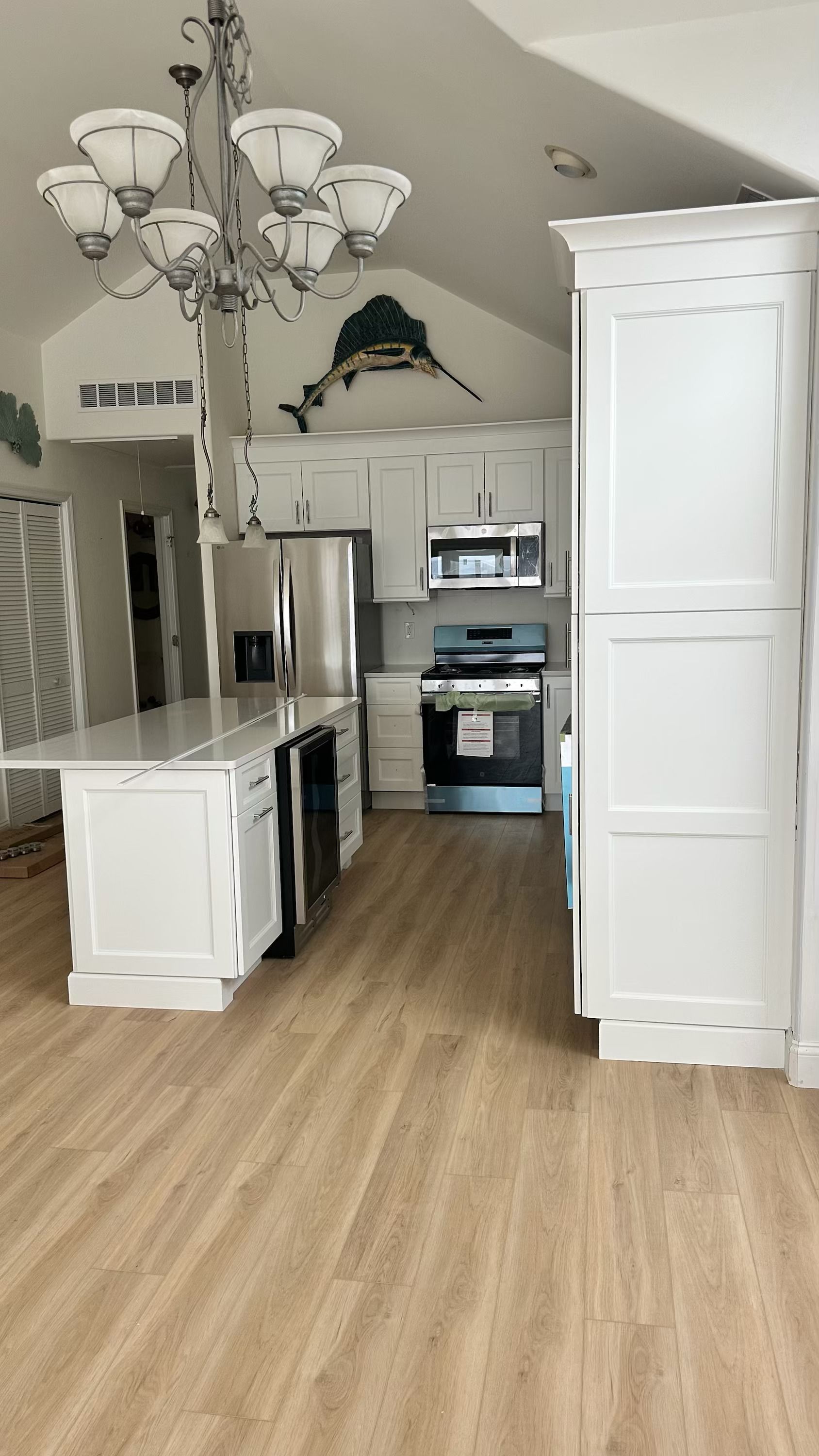 A kitchen with white cabinets , stainless steel appliances , hardwood floors and a chandelier.