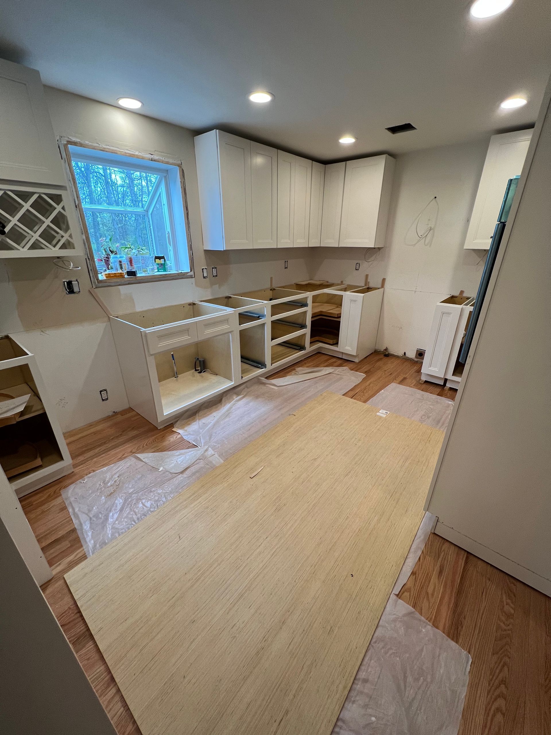 A kitchen under construction with white cabinets and wooden floors.