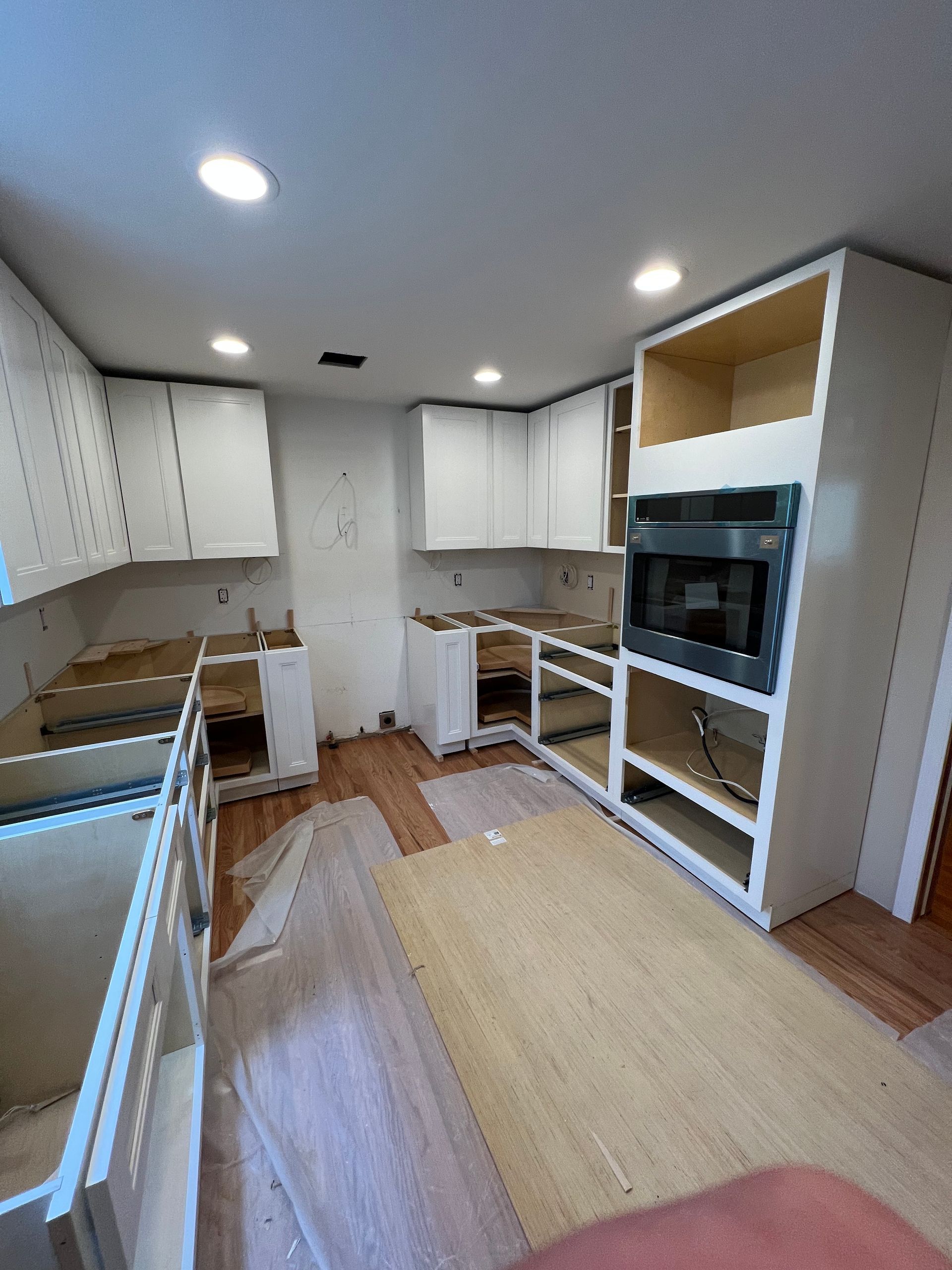 A kitchen with white cabinets and wooden floors is being remodeled.