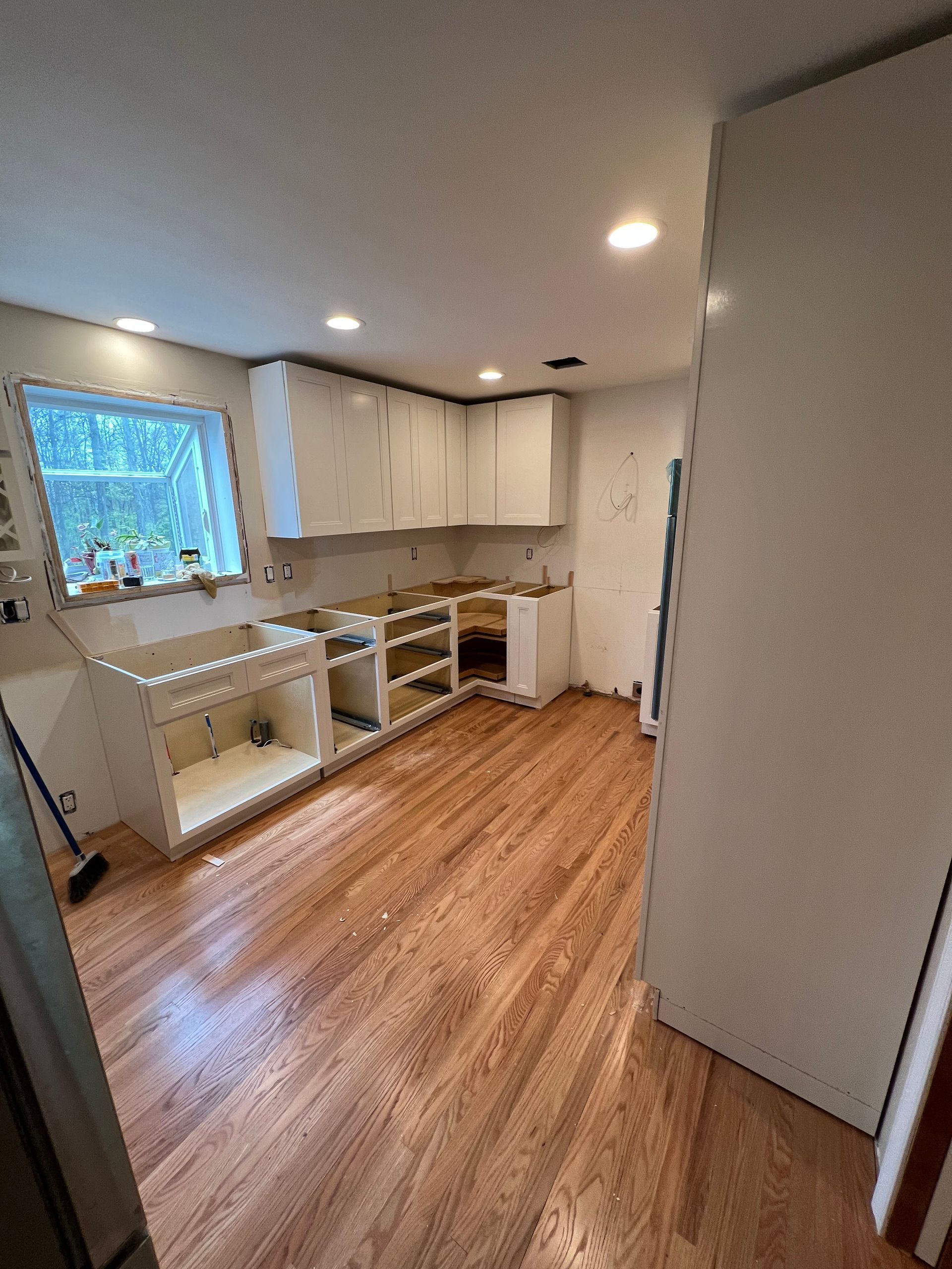 A kitchen with hardwood floors and white cabinets is being remodeled.