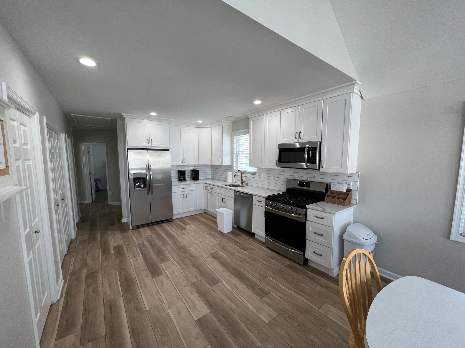A kitchen with white cabinets , stainless steel appliances , hardwood floors and a table.