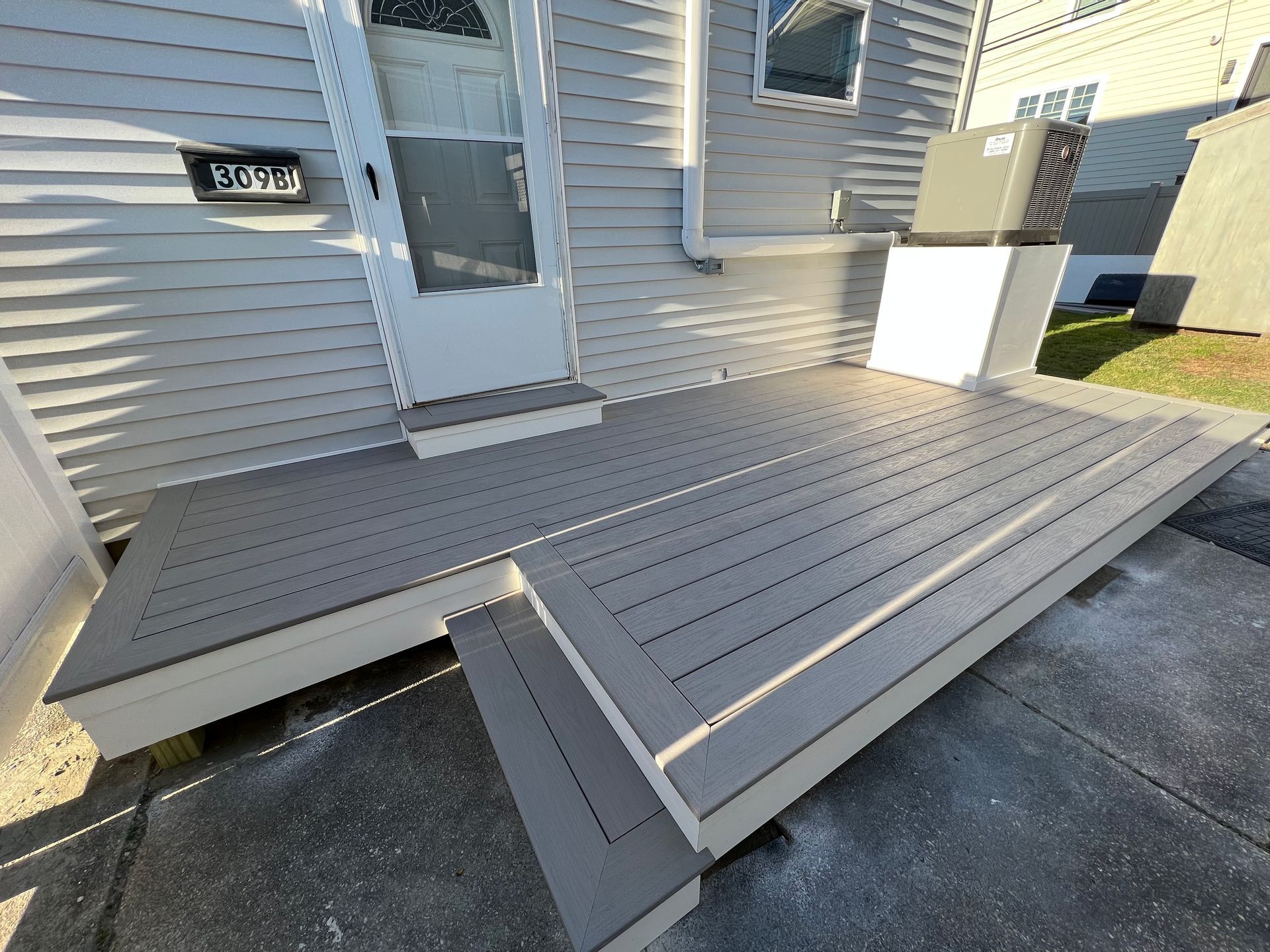 A gray deck is sitting in front of a white house.