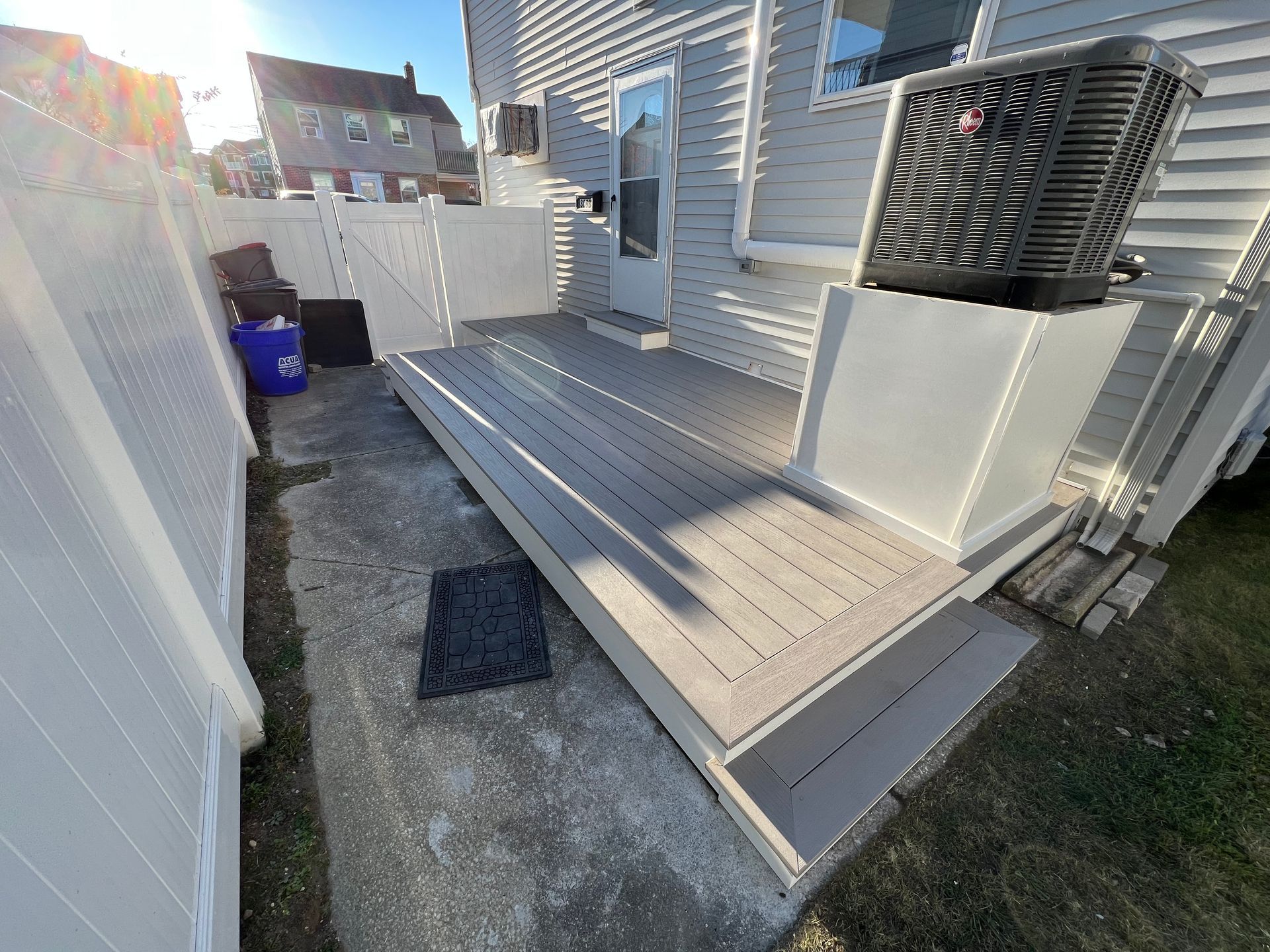 A deck with stairs leading up to a house next to a white fence.