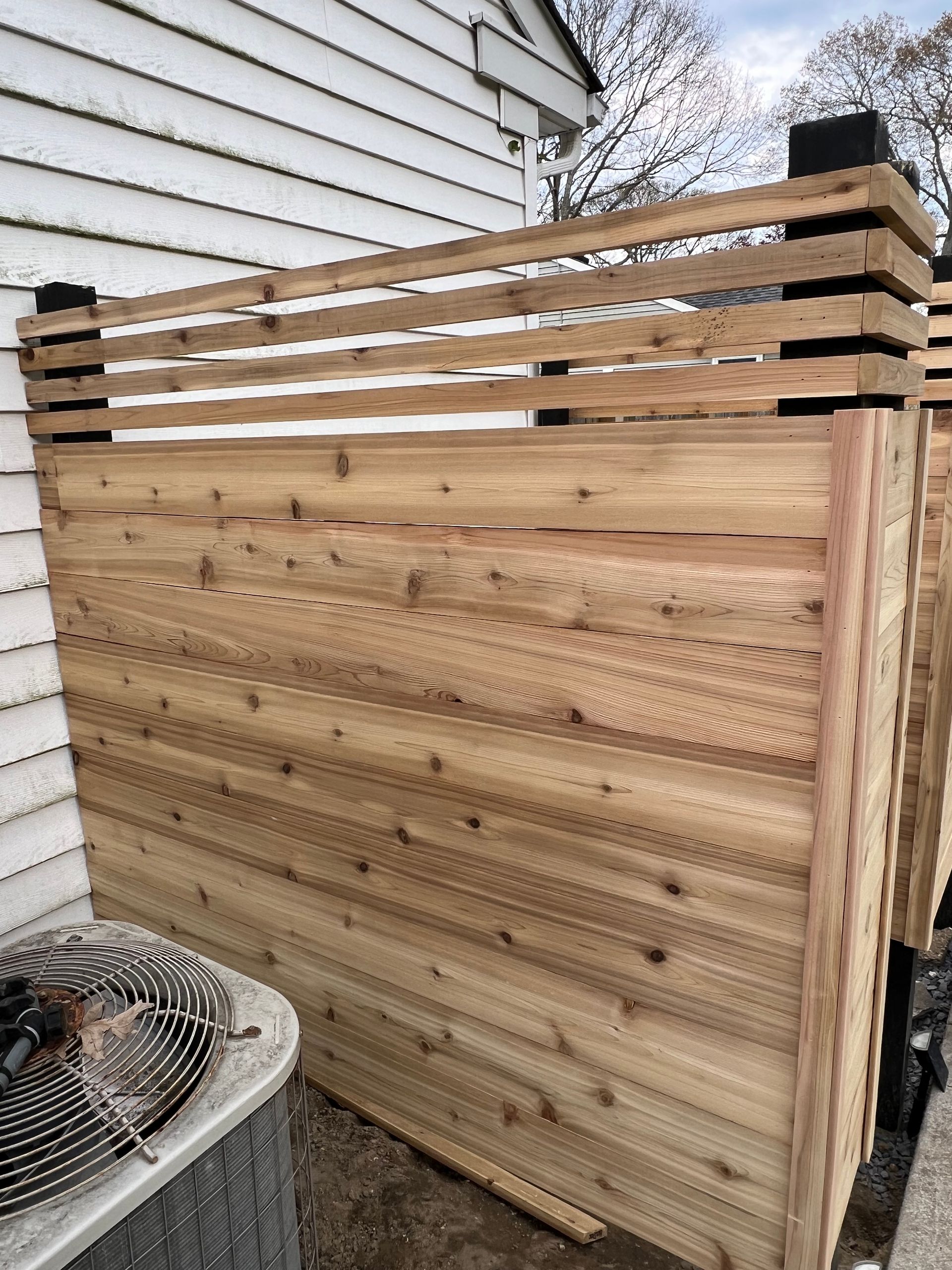A wooden fence is sitting in front of a house next to an air conditioner.