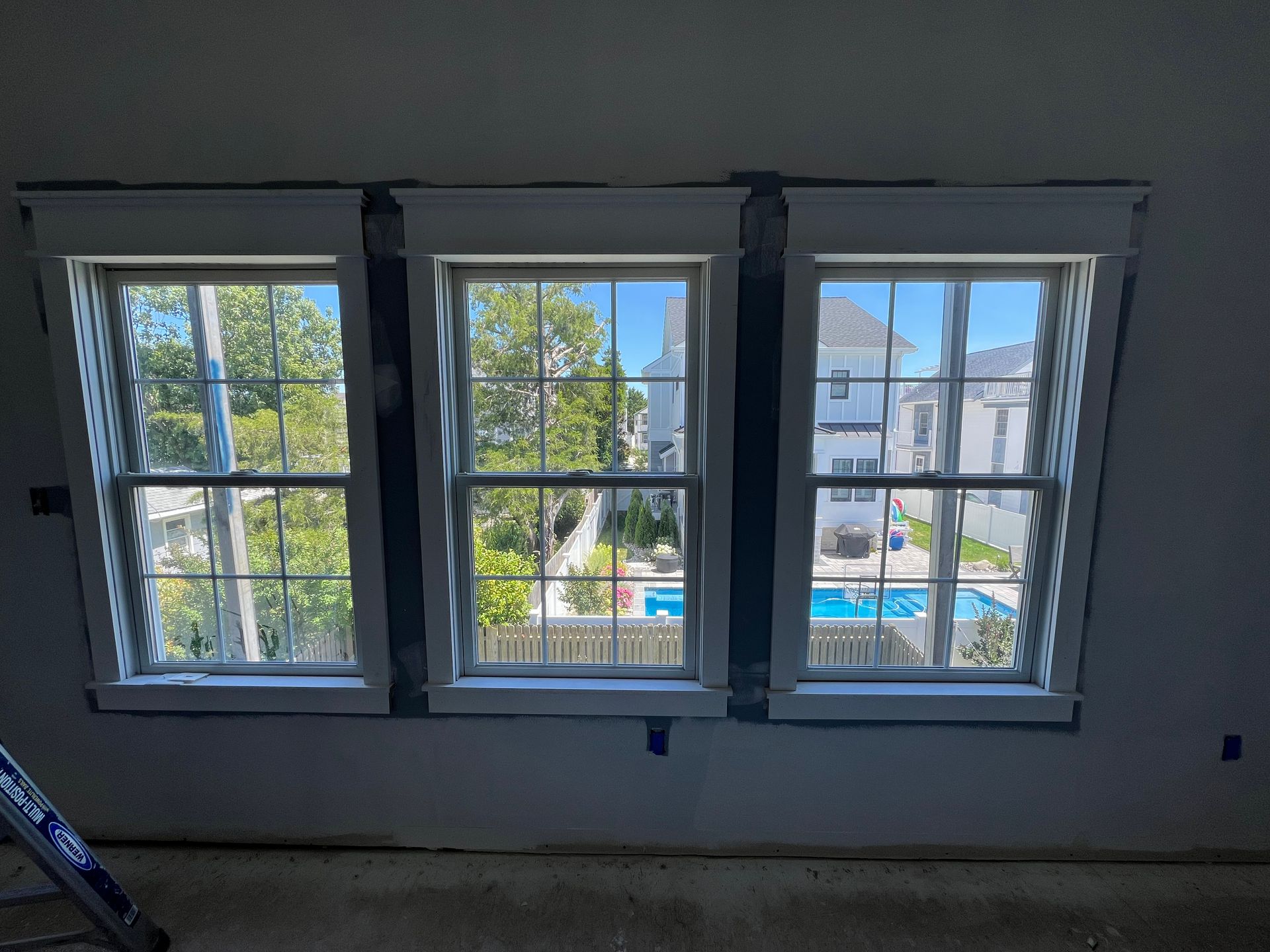 Three windows in a room with a view of a house and a pool.
