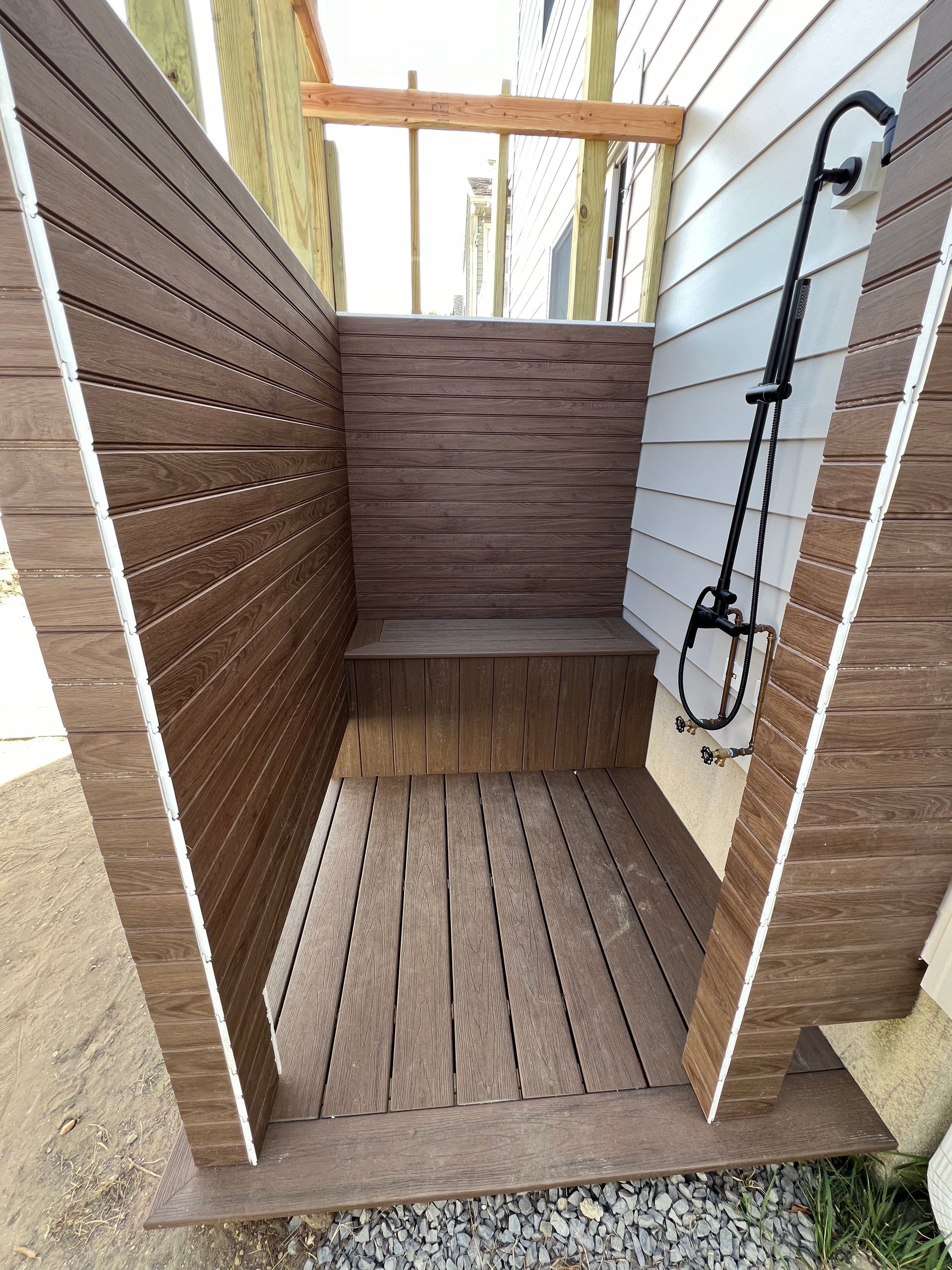 A wooden outdoor shower with a bench and a shower head