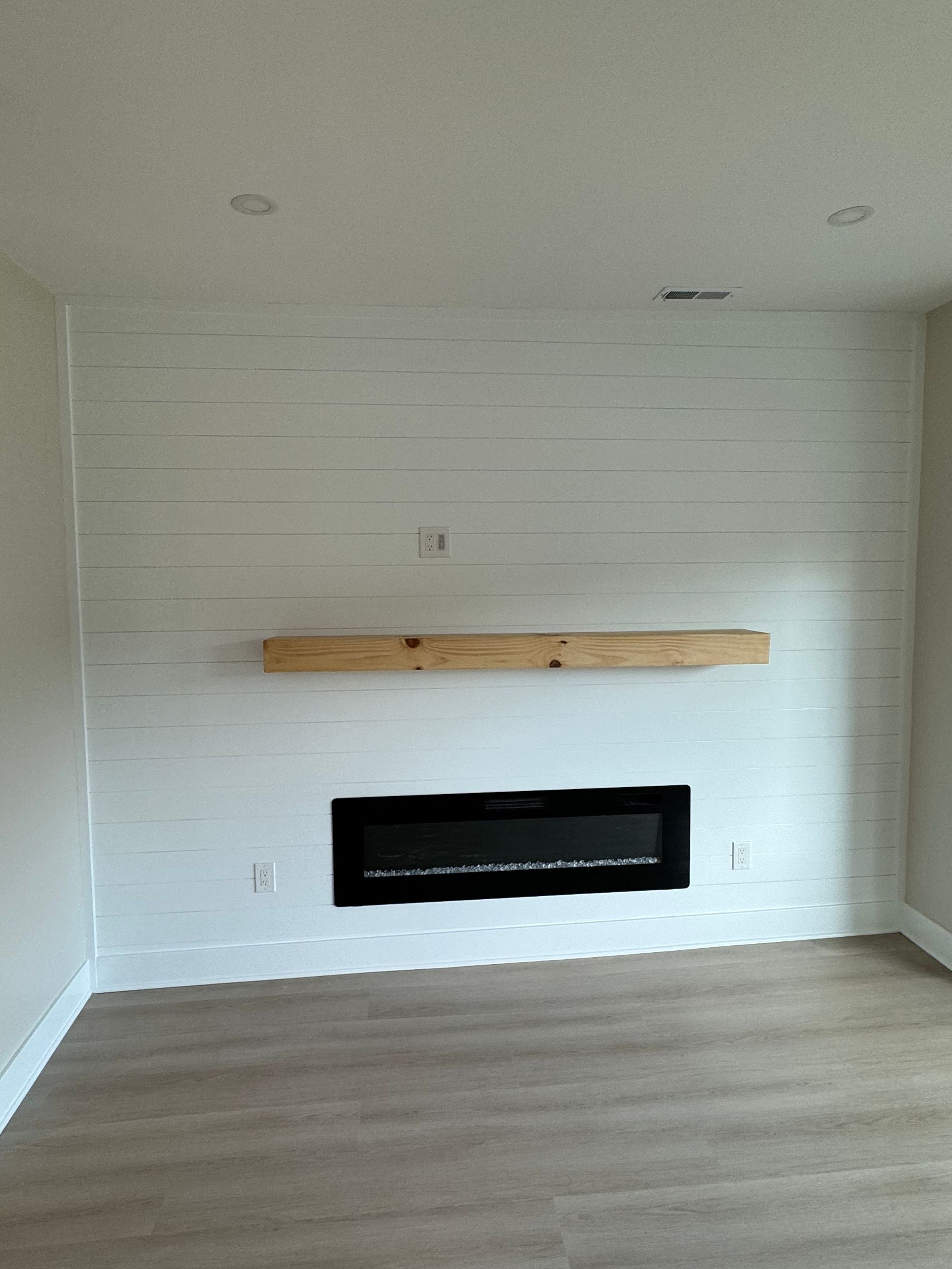 An empty living room with a fireplace and a wooden shelf