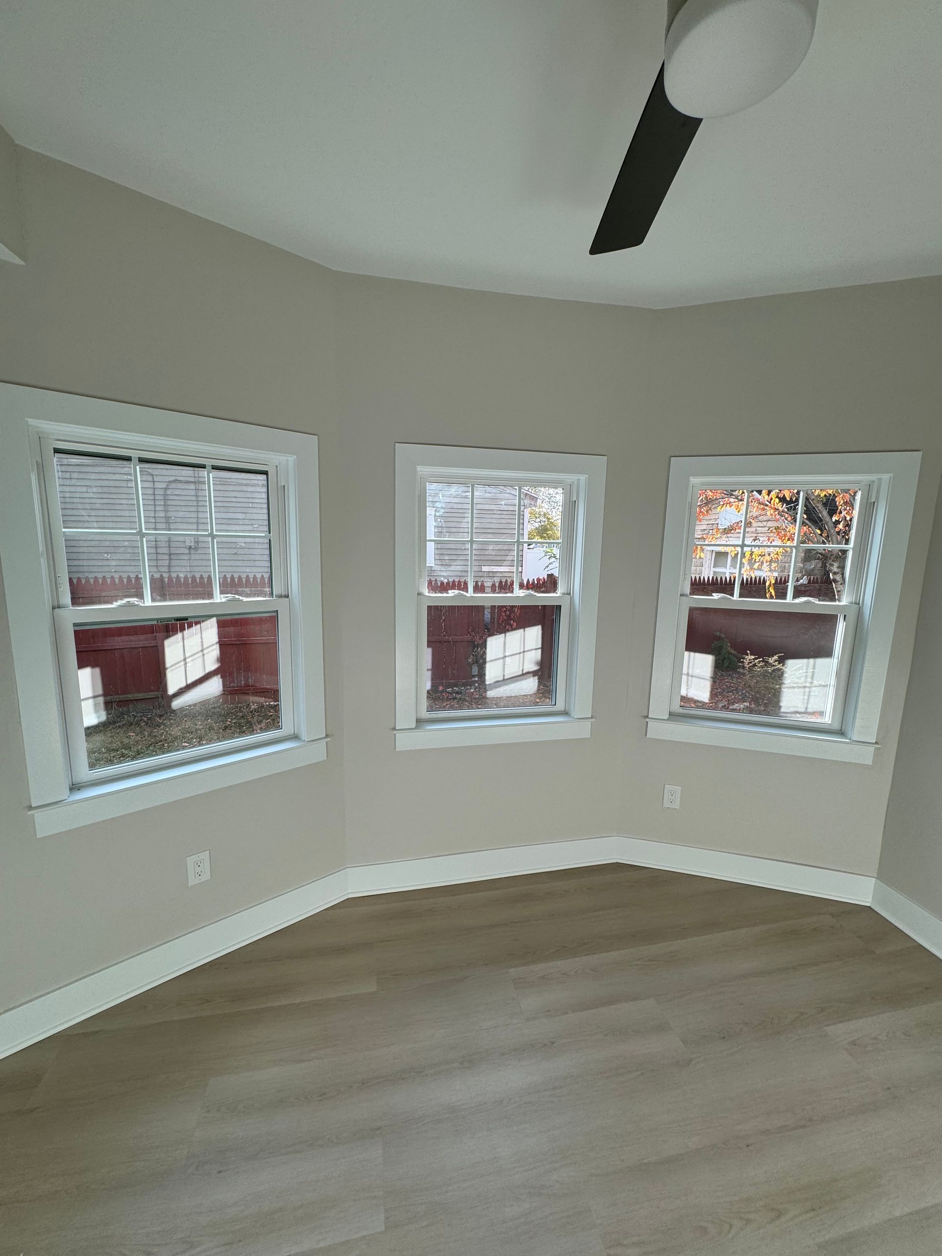 An empty room with three windows and a ceiling fan.