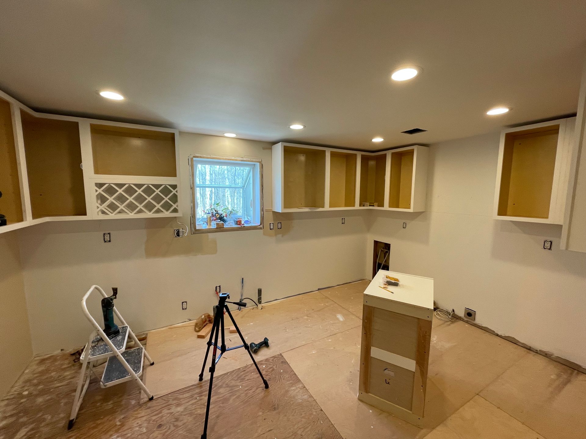 A kitchen under construction with a ladder and a tripod.