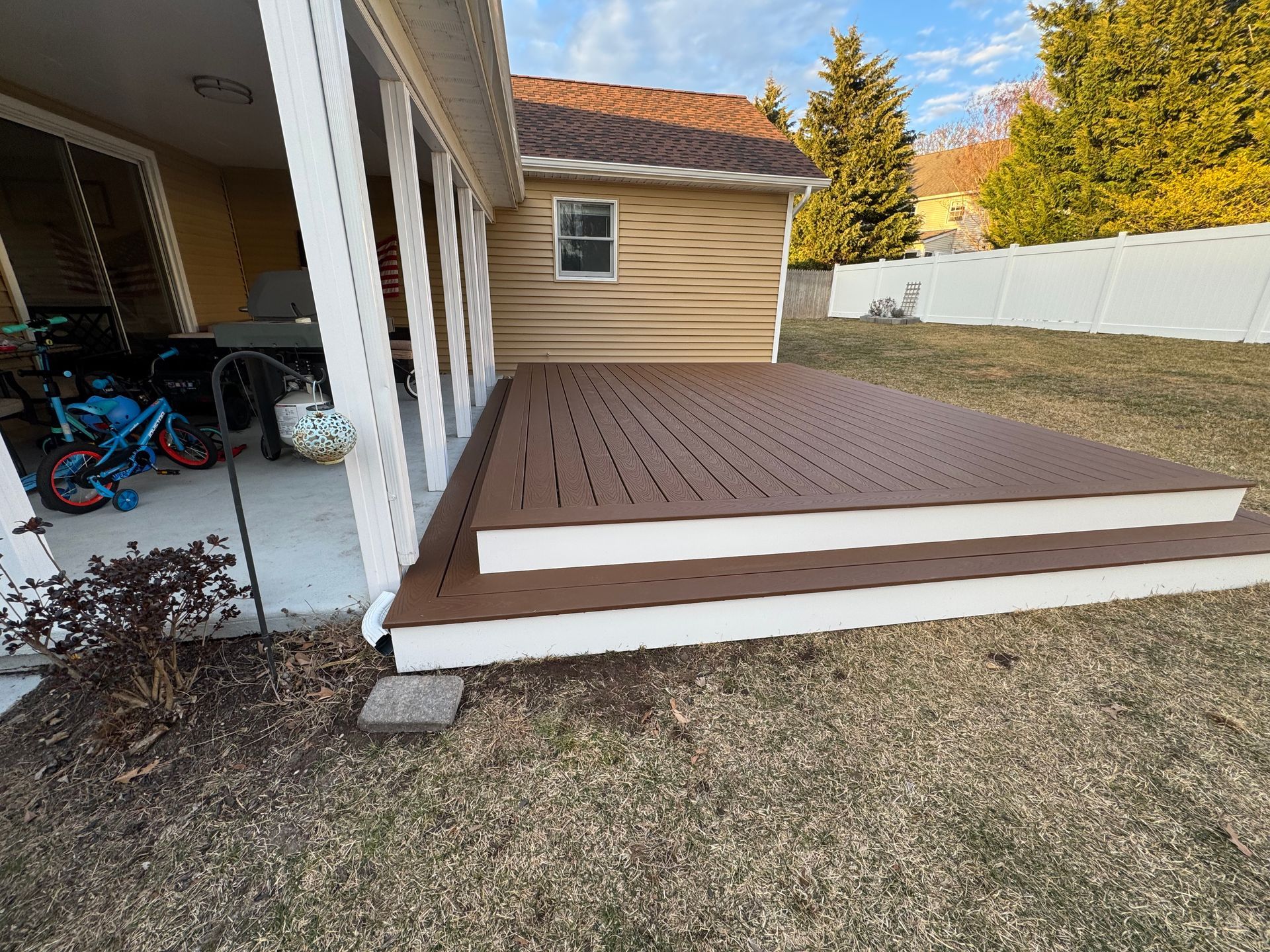 A wooden deck with stairs leading up to it is in the backyard of a house.