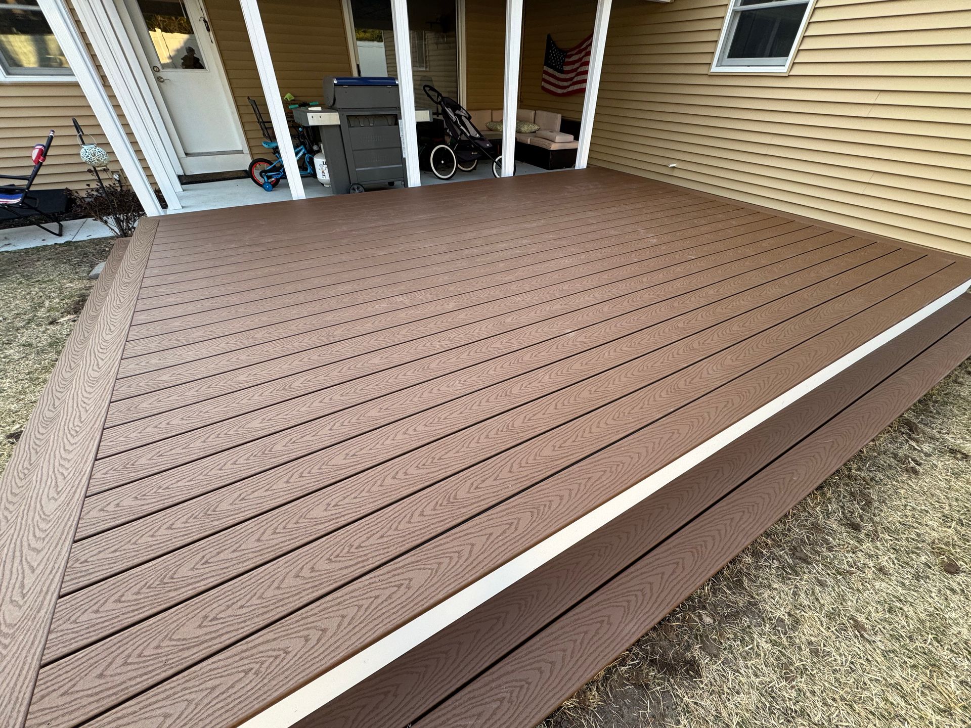 A brown deck with a white border is in front of a house.