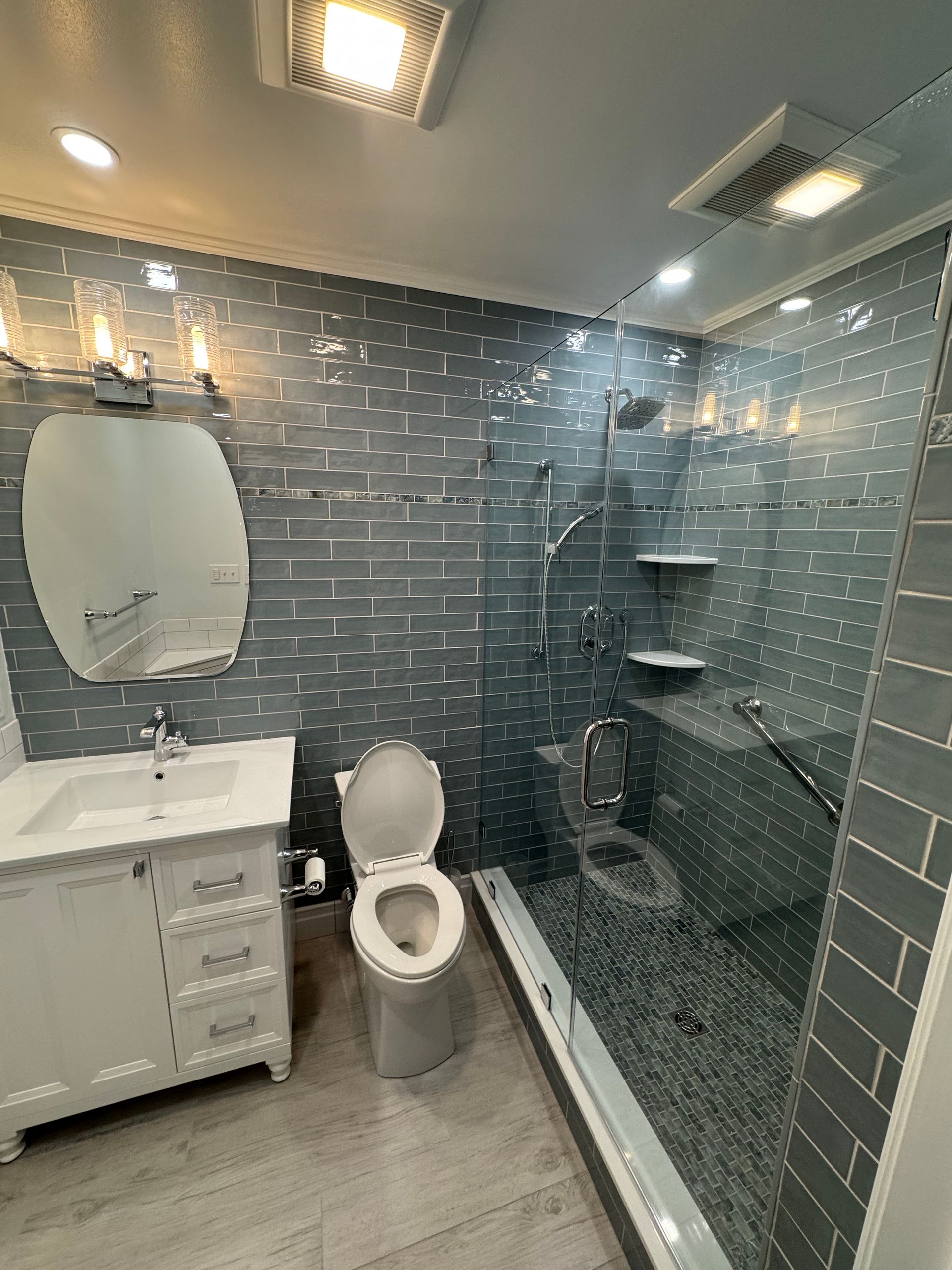 A bathroom with a toilet , sink , mirror and walk in shower.