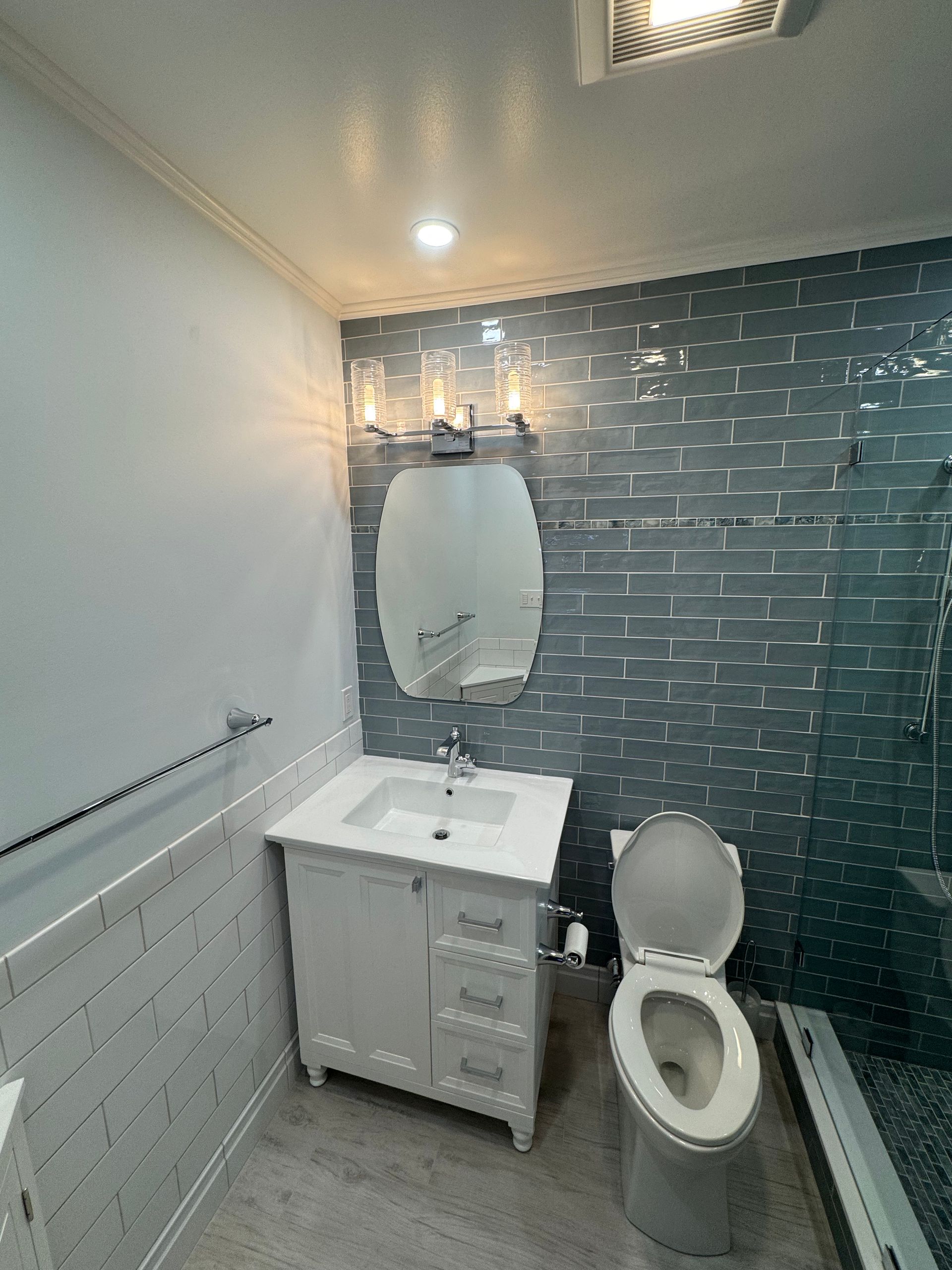 A bathroom with a toilet , sink , mirror and shower.