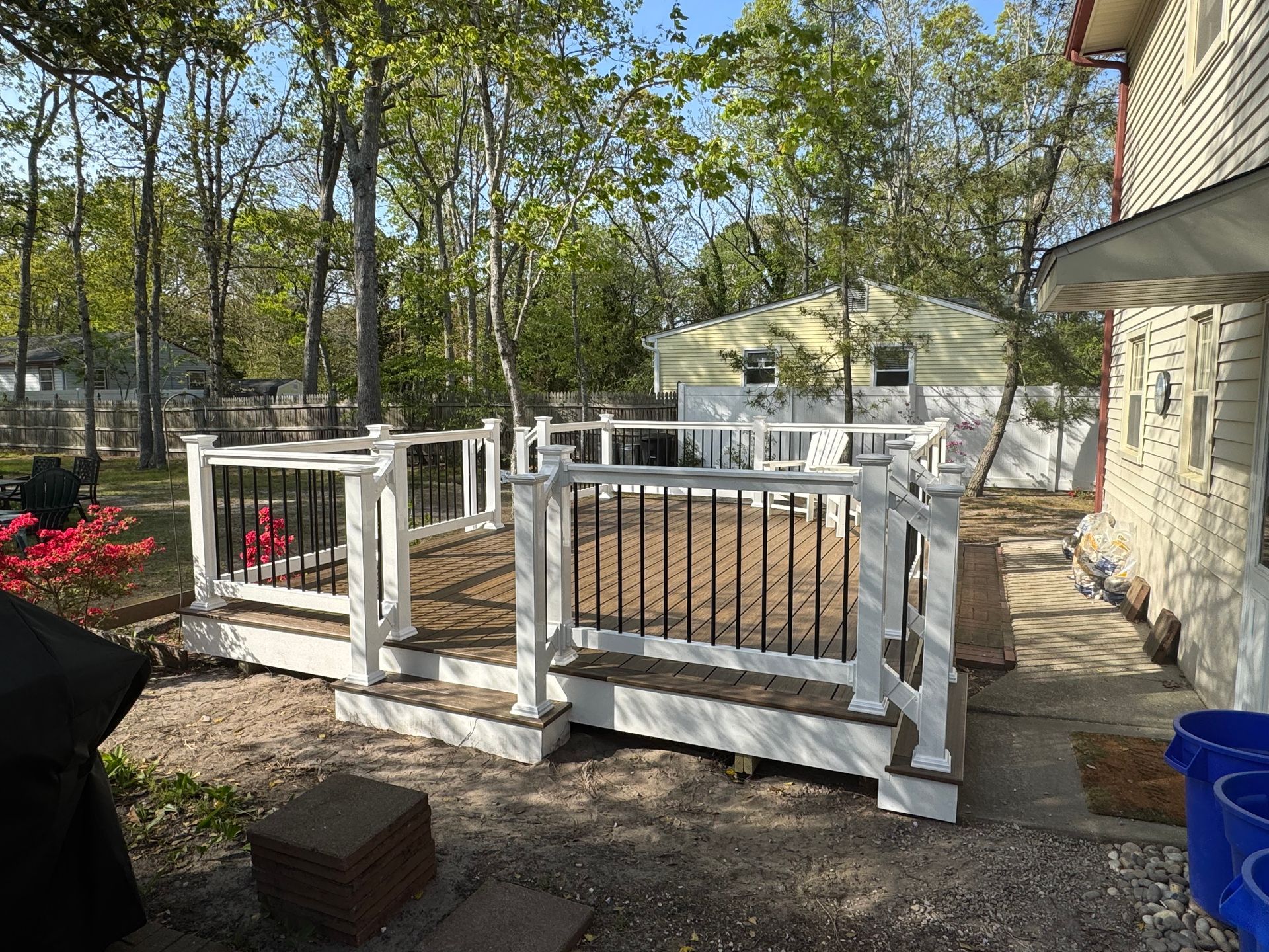 A large deck with a white railing is in the backyard of a house.