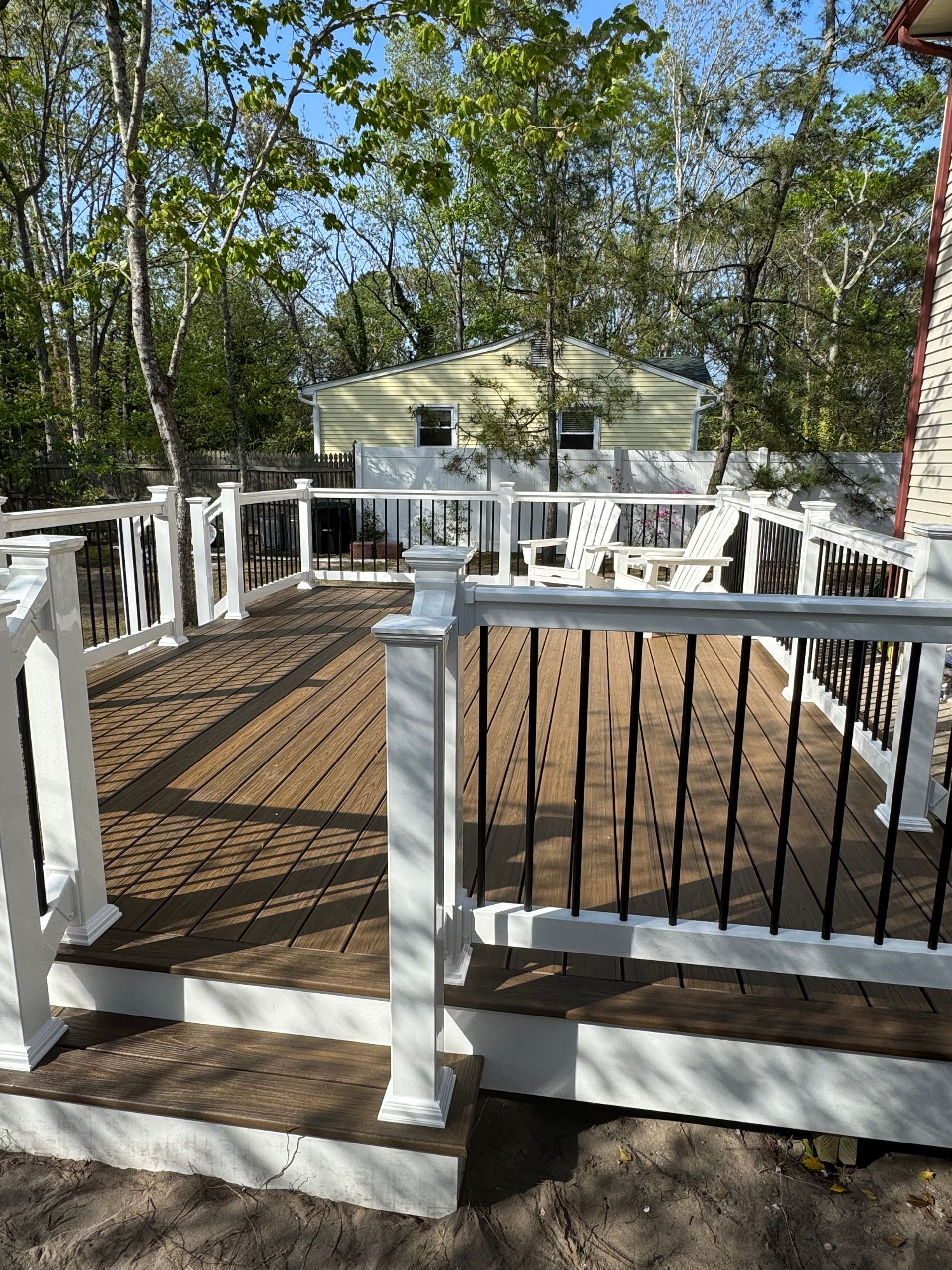 A wooden deck with a white railing and chairs on it.