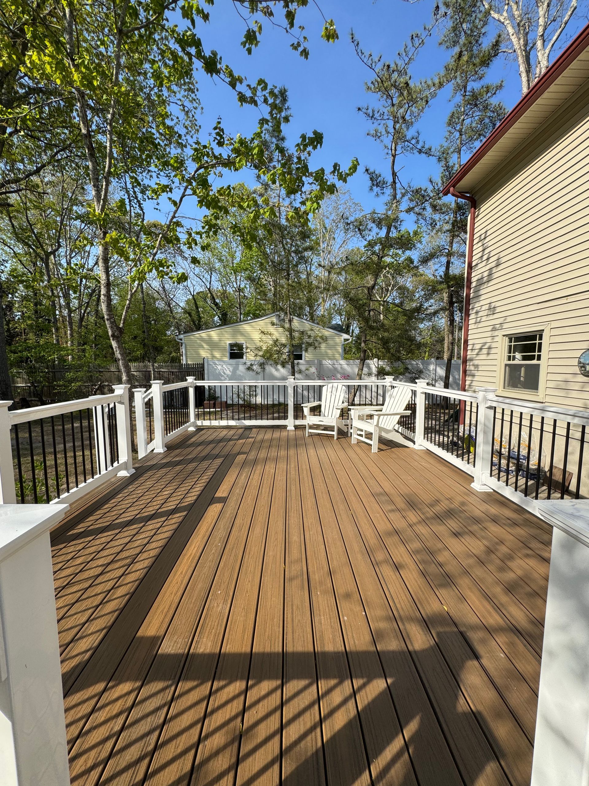 A large wooden deck with a white railing and chairs