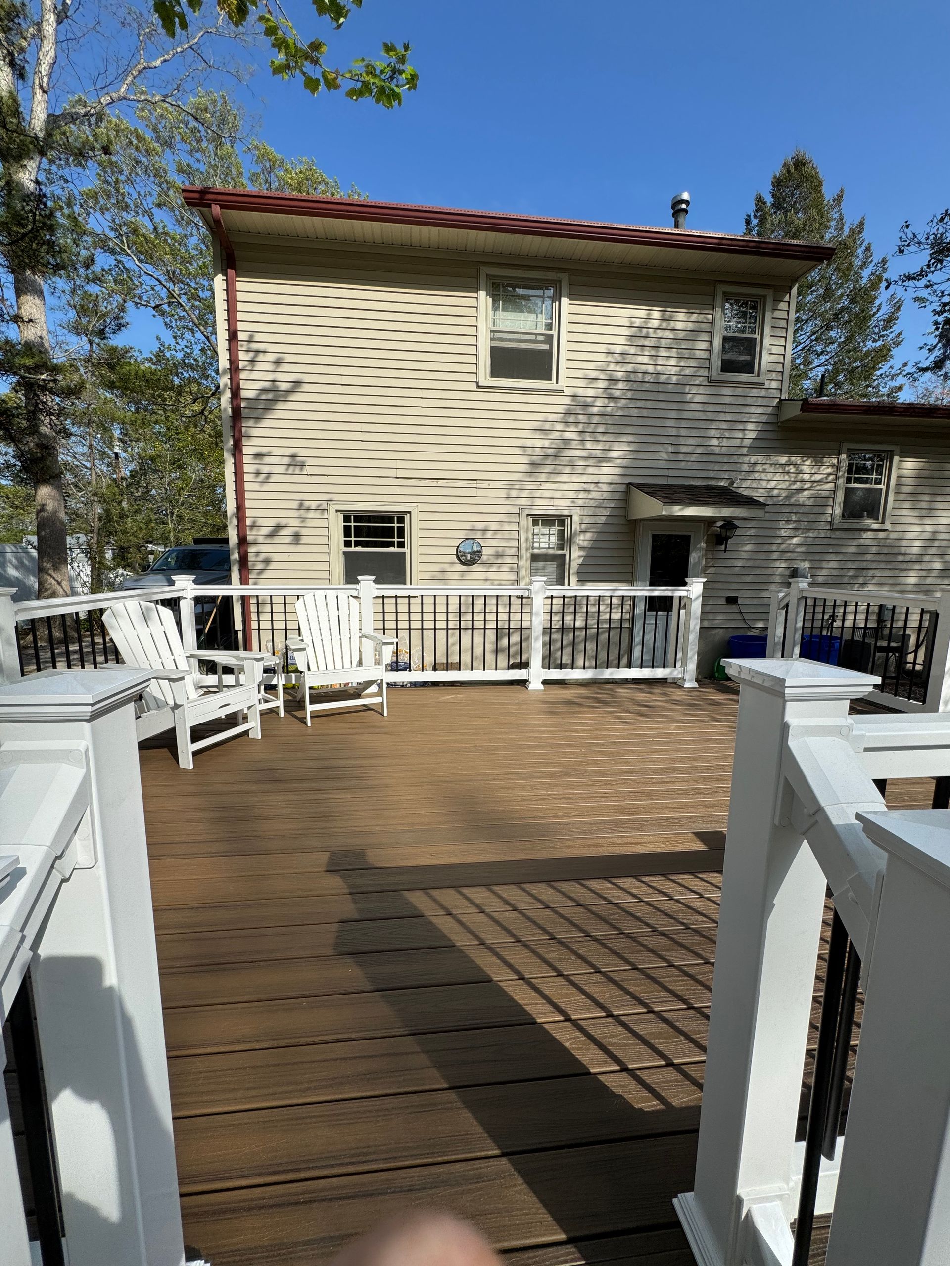 A wooden deck with chairs and a fence in front of a house.