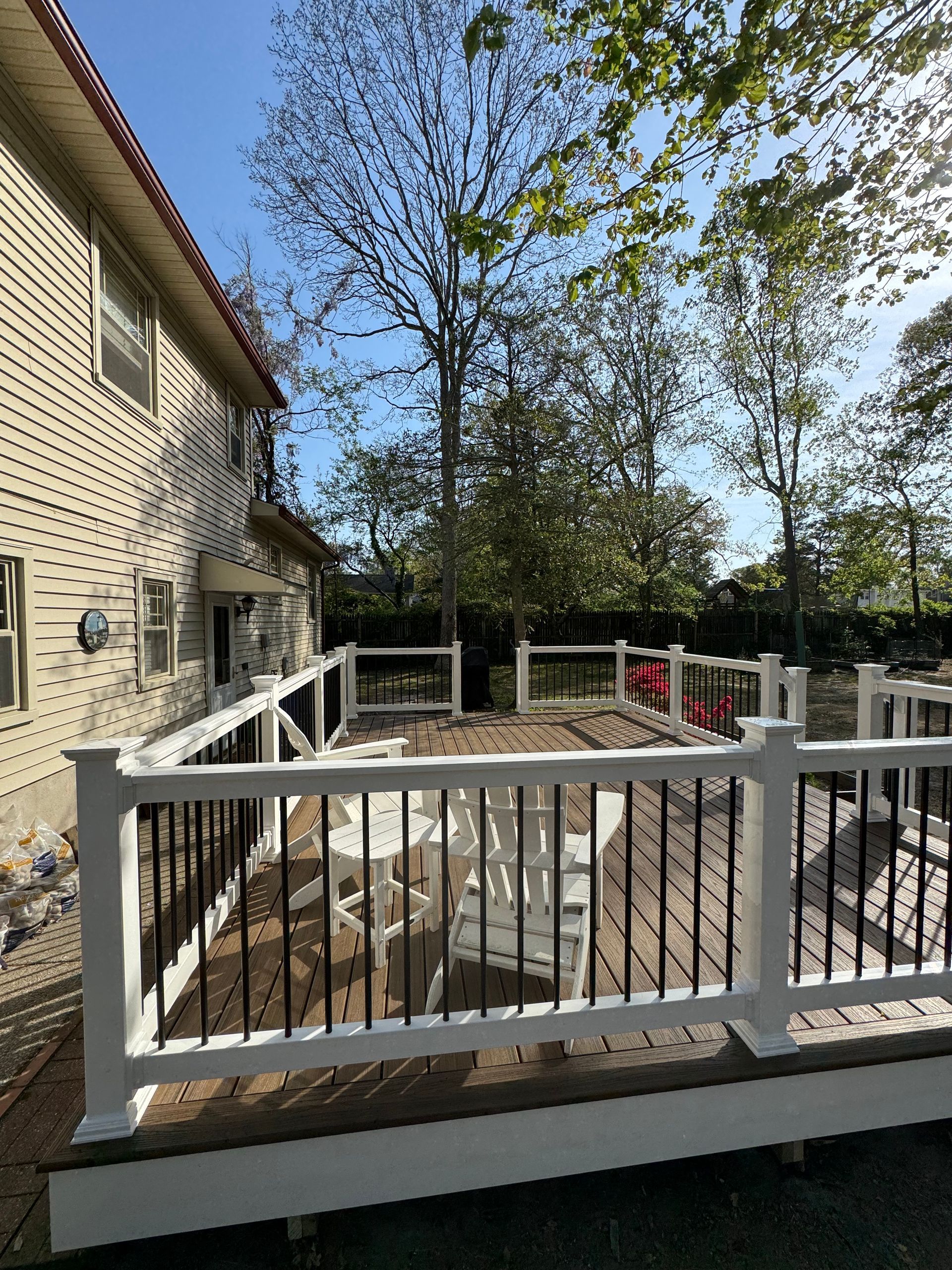 A wooden deck with a white railing and chairs in front of a house.