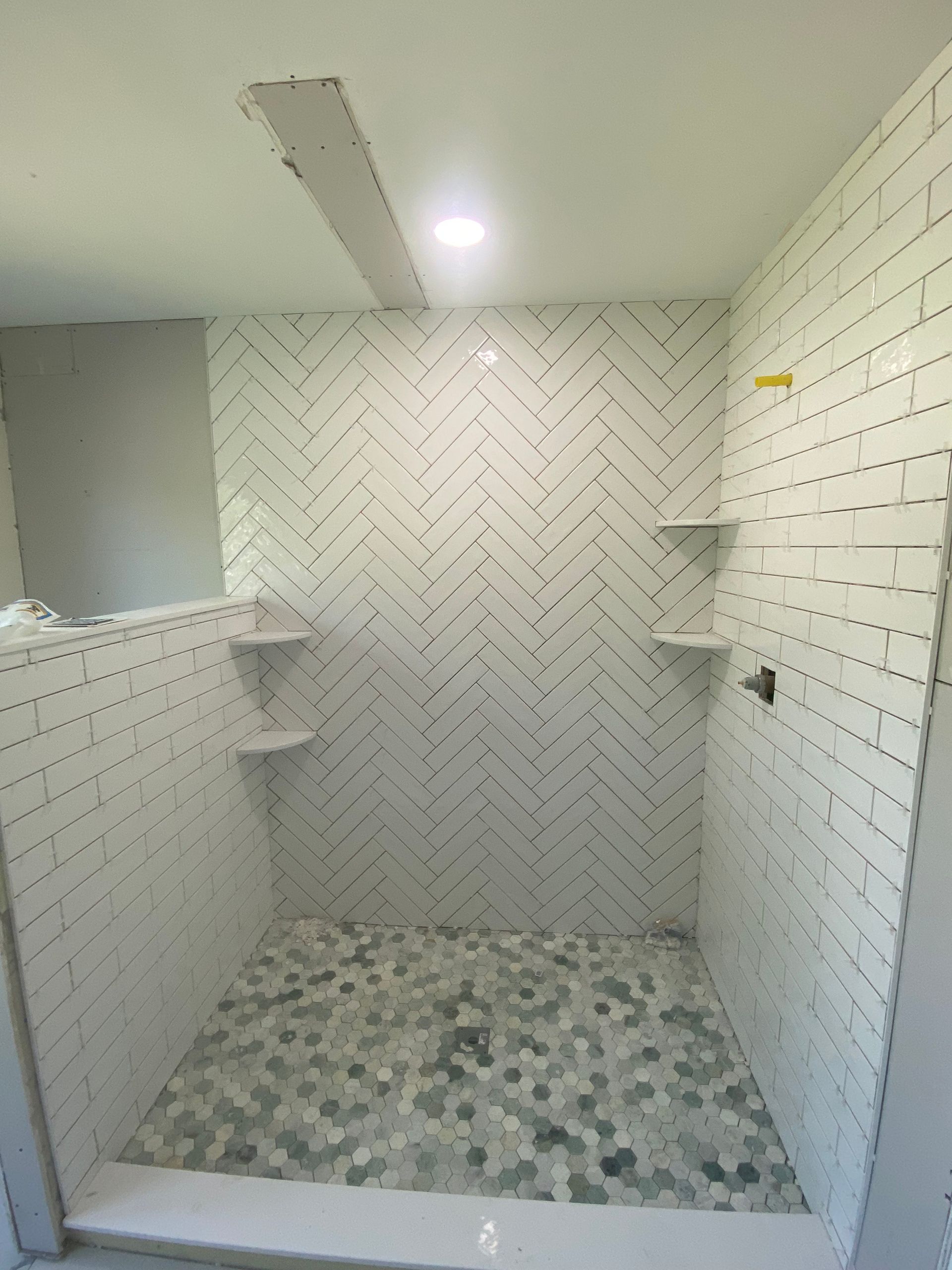 A shower with white tiles and a herringbone pattern on the wall.