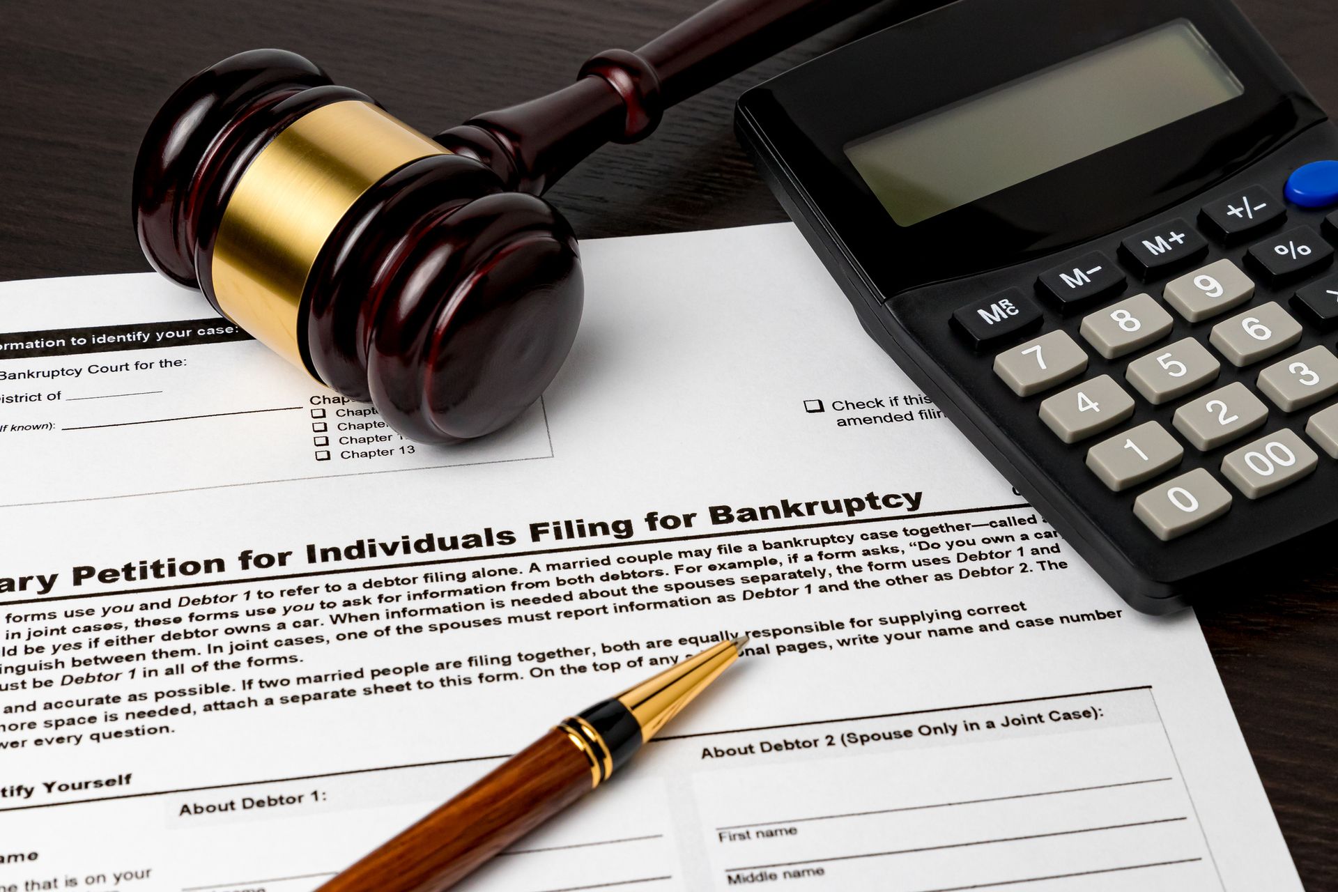 Gavel, calculator, and pen on bankruptcy petition form.