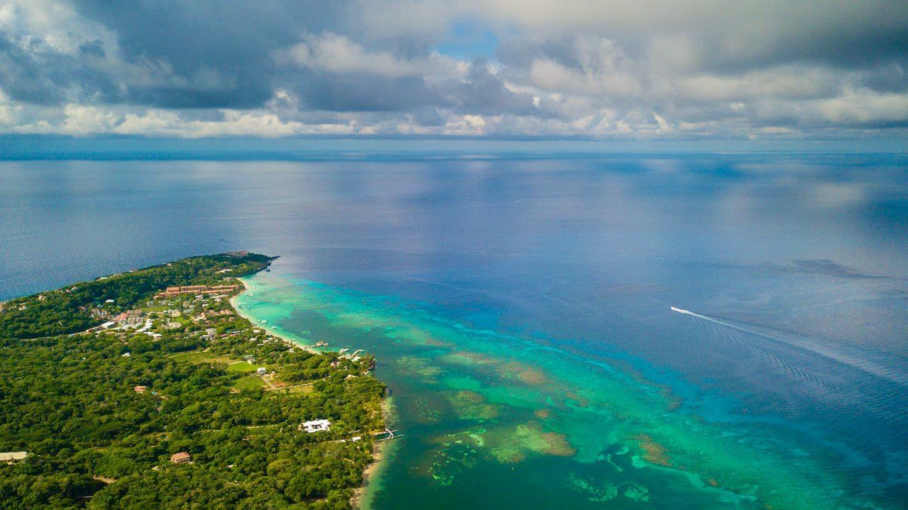 Aerial view of island with lush green vegetation, turquoise water, and cloudy sky.