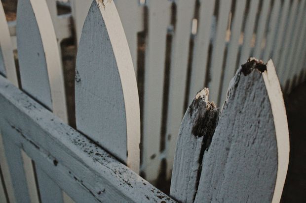 Close-up of a white picket fence; one broken picket.