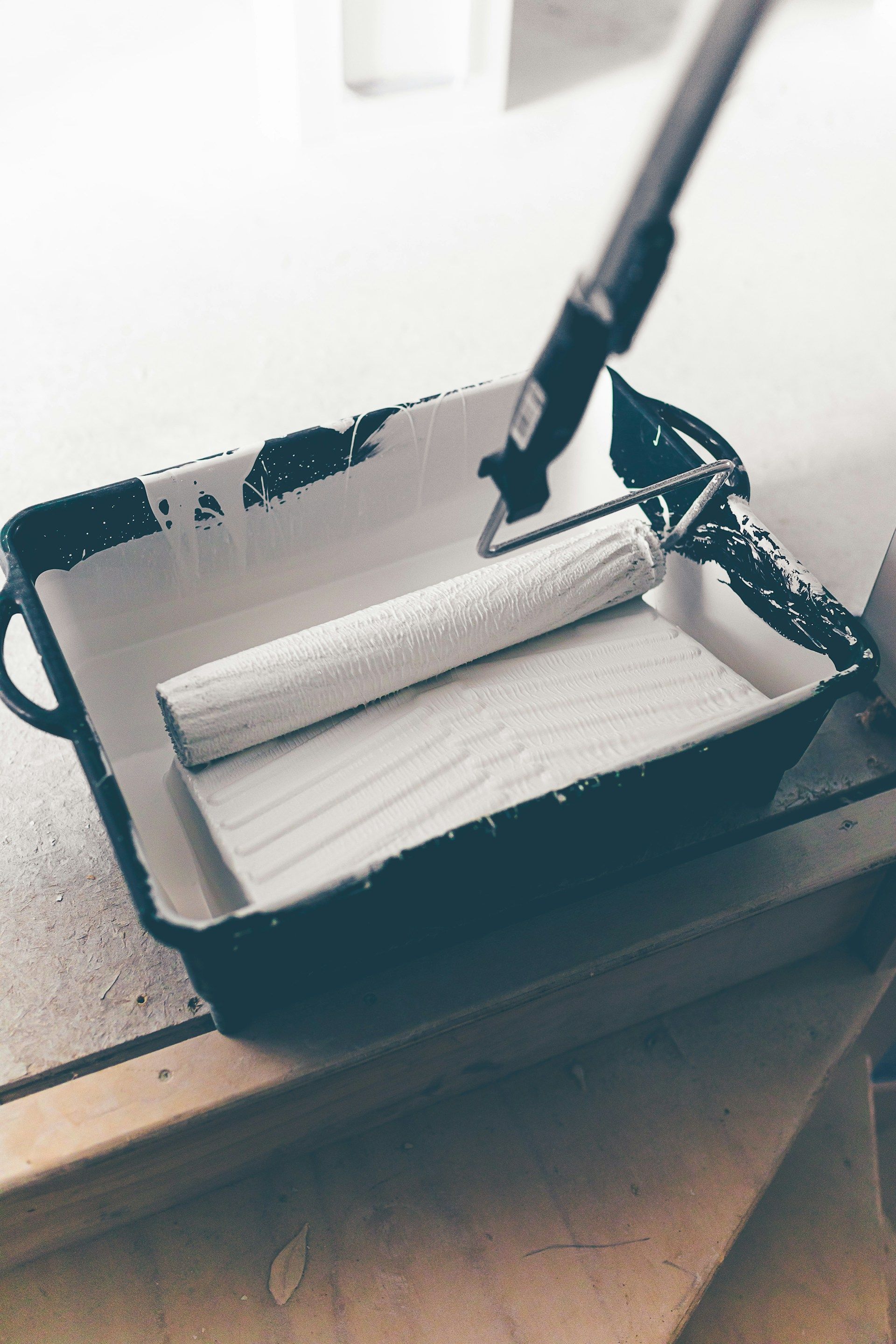 Paint tray with roller, white paint, and extended handle; indoors.