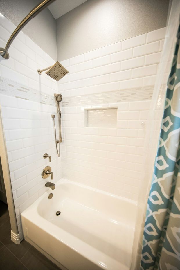 White shower with gold fixtures and a teal patterned shower curtain.