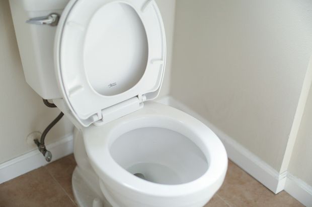 White toilet with the lid up, in a bathroom setting.