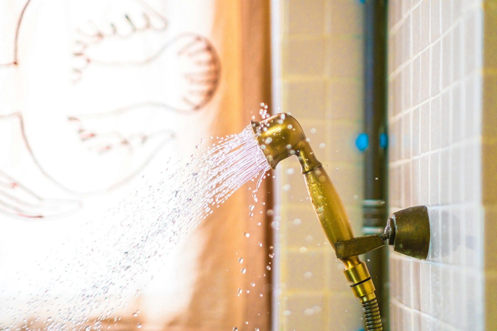 Gold showerhead spraying water in a tiled shower stall.