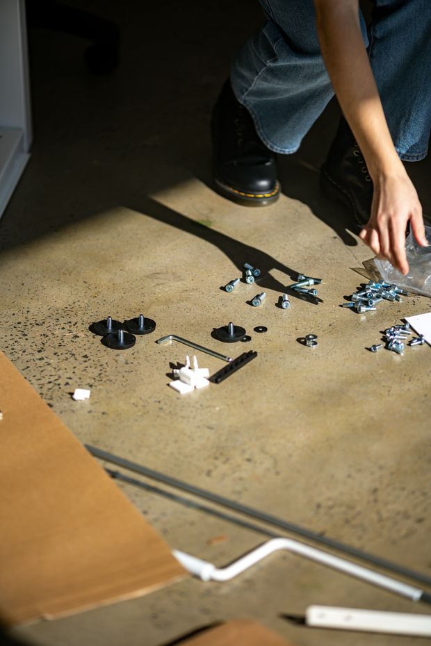 Person assembling furniture on a concrete floor, scattering screws and parts.