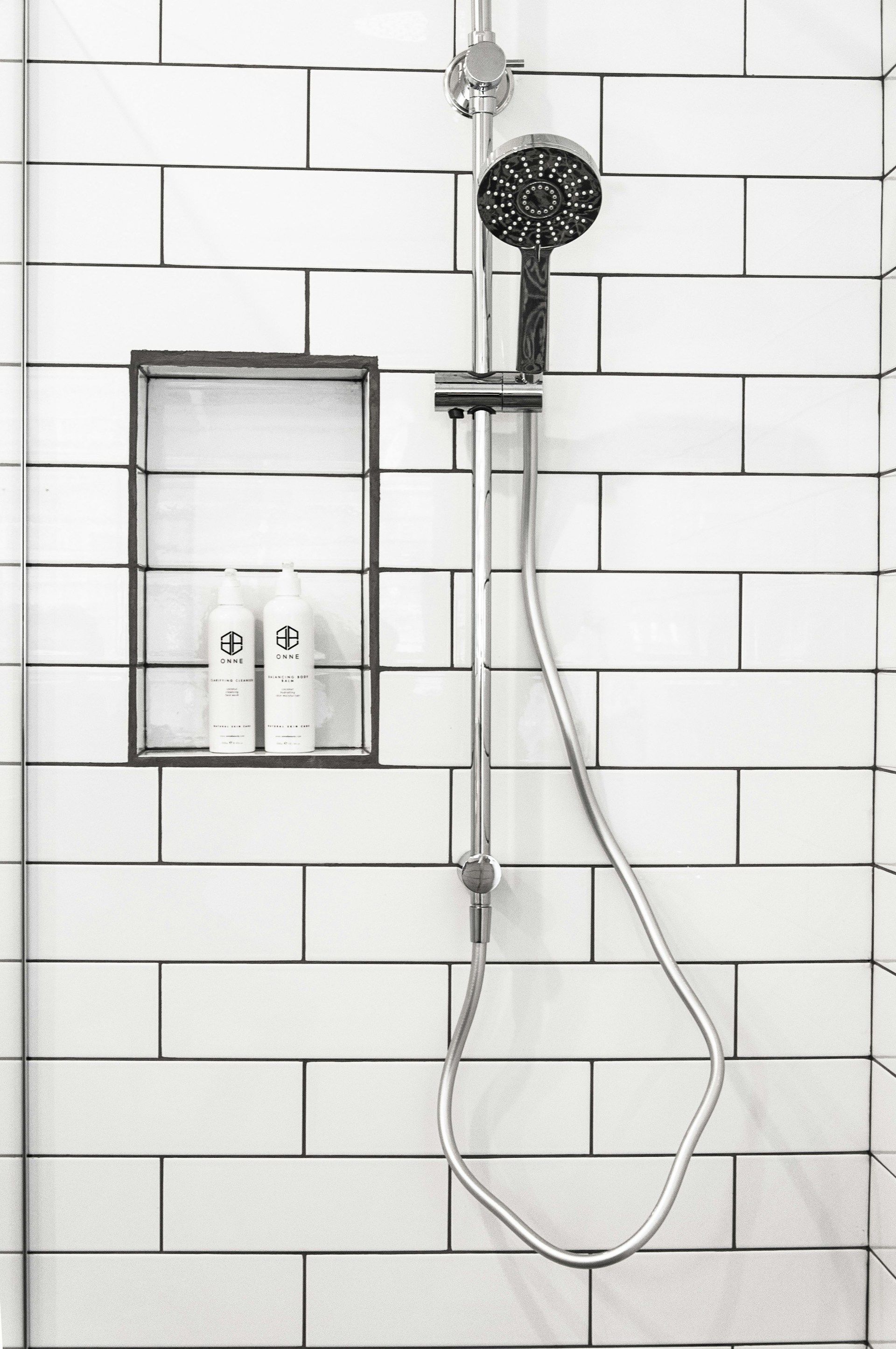 Shower with white subway tile, built-in shelf with toiletries, and a handheld showerhead.