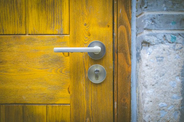 Yellow wooden door with silver handle and keyhole, next to a stone wall.