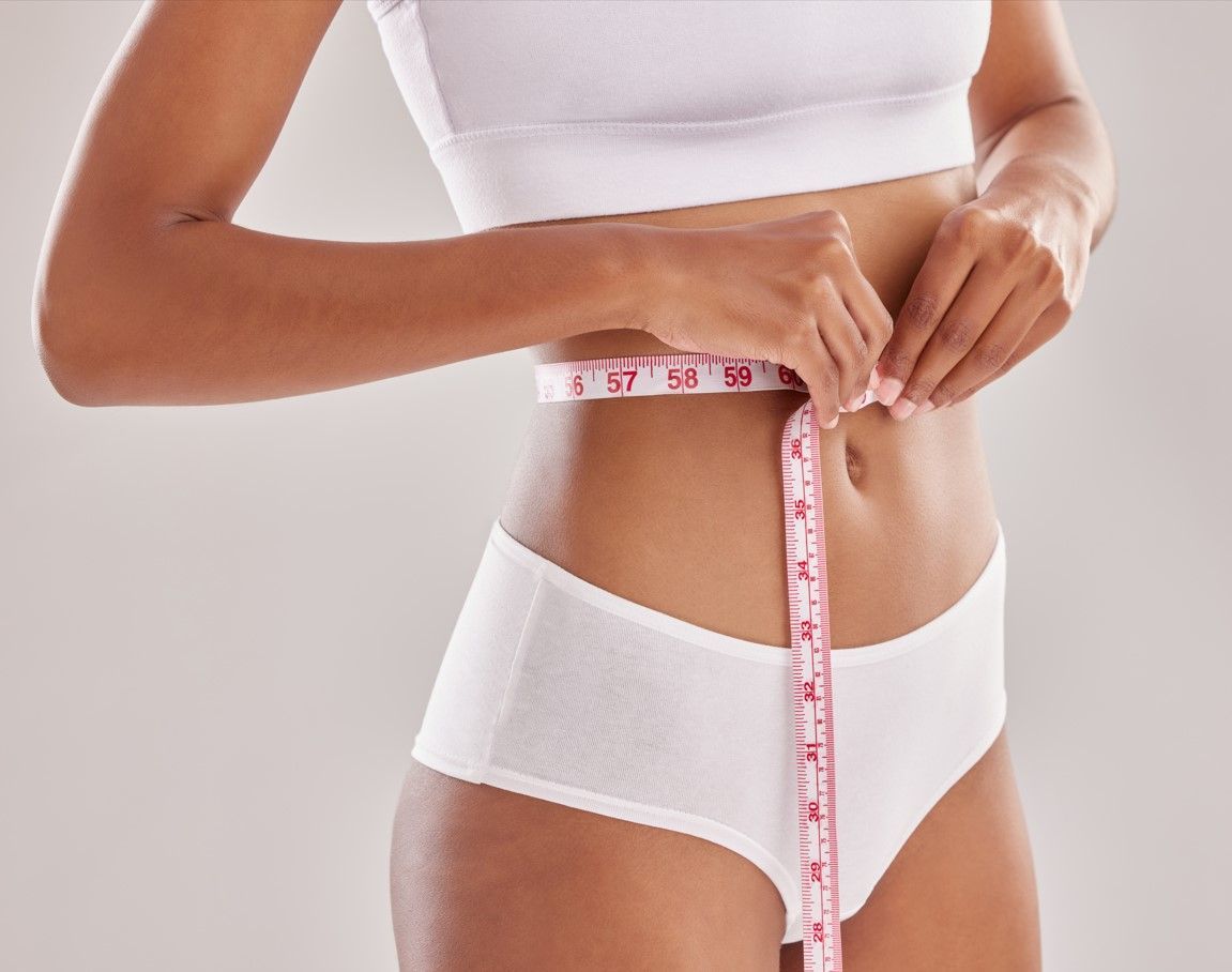 A woman is measuring her waist with a tape measure.