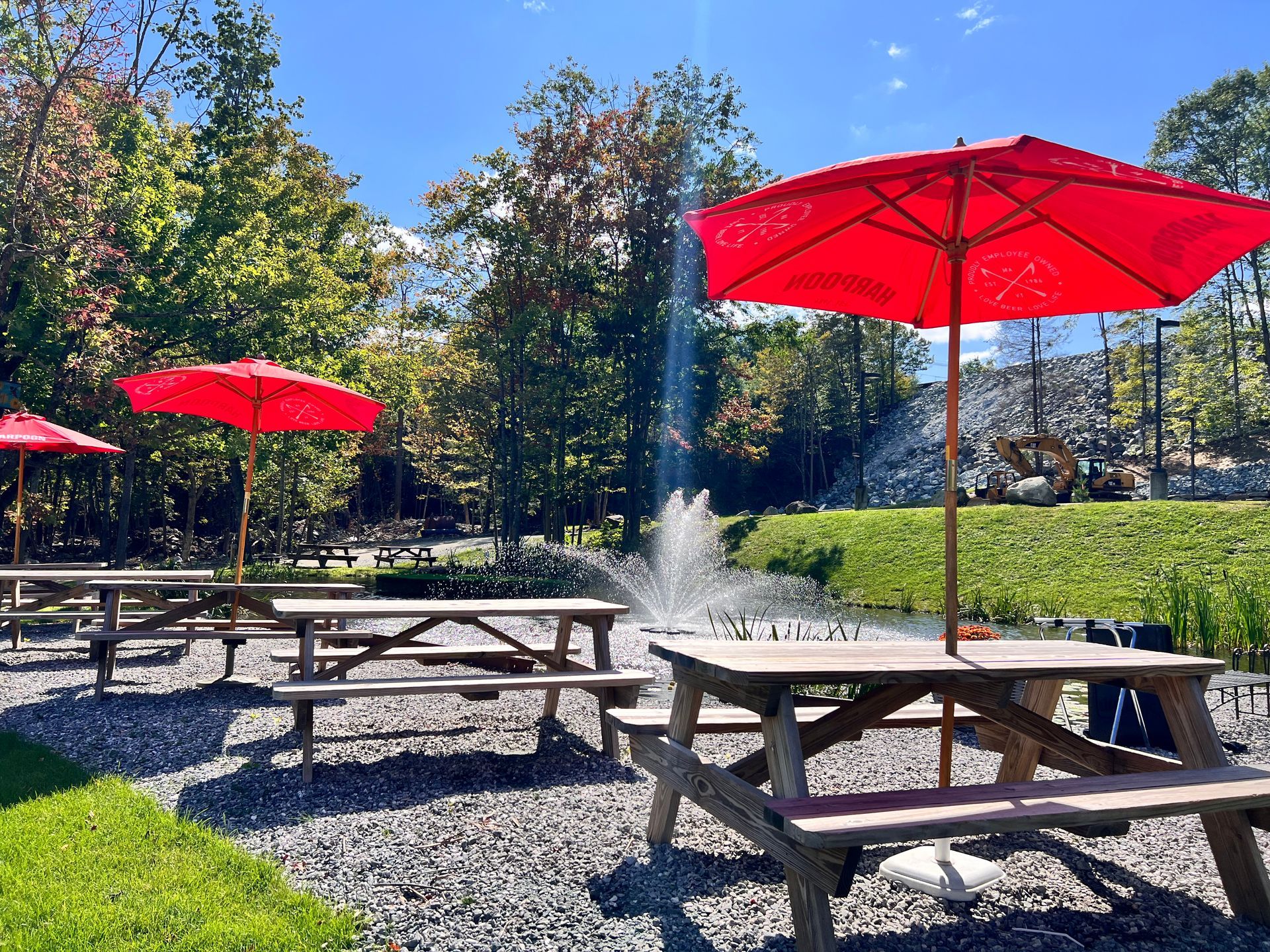 A row of picnic tables with red umbrellas and a fountain in the background.