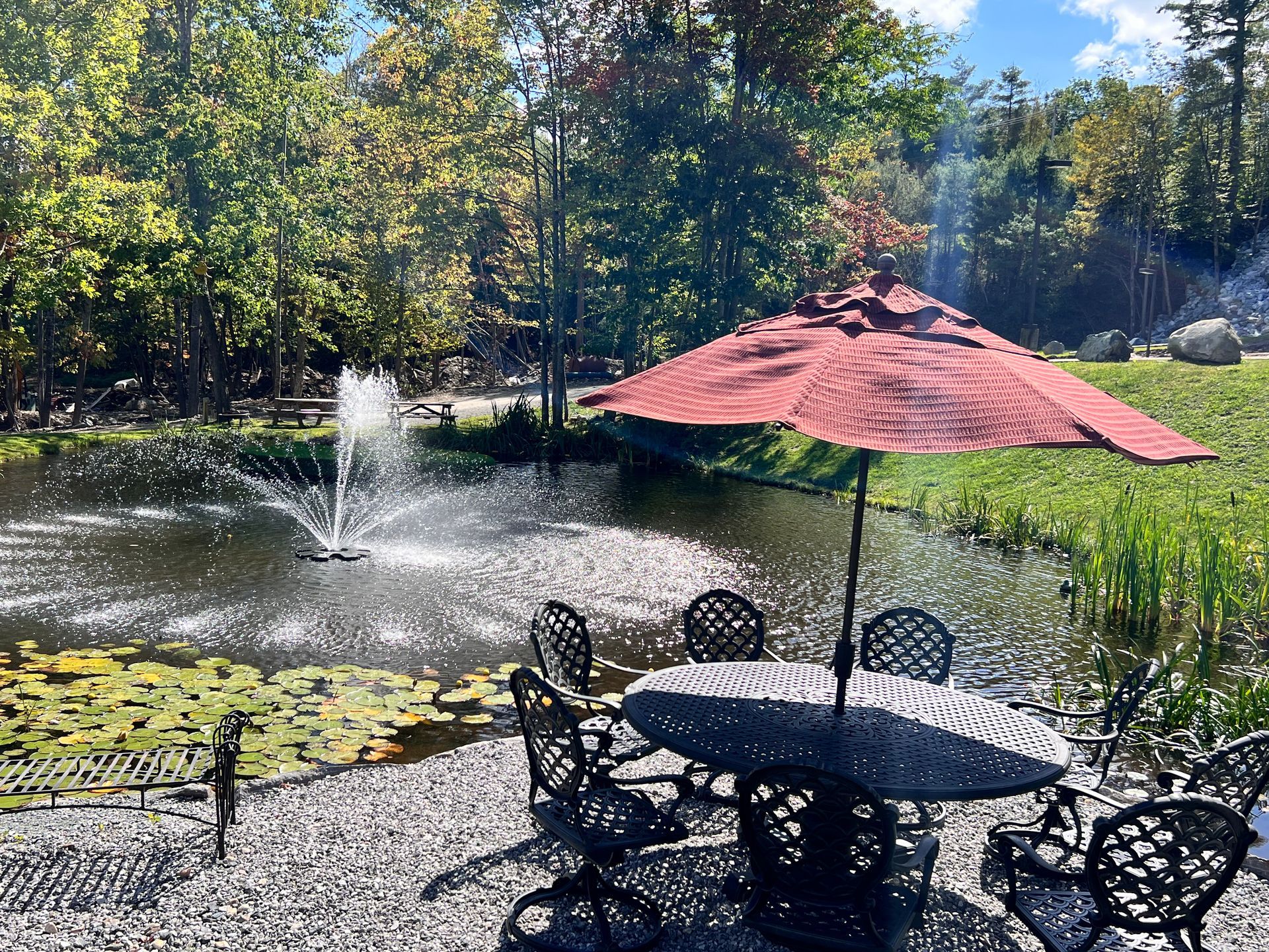 A table and chairs under an umbrella in front of a pond.
