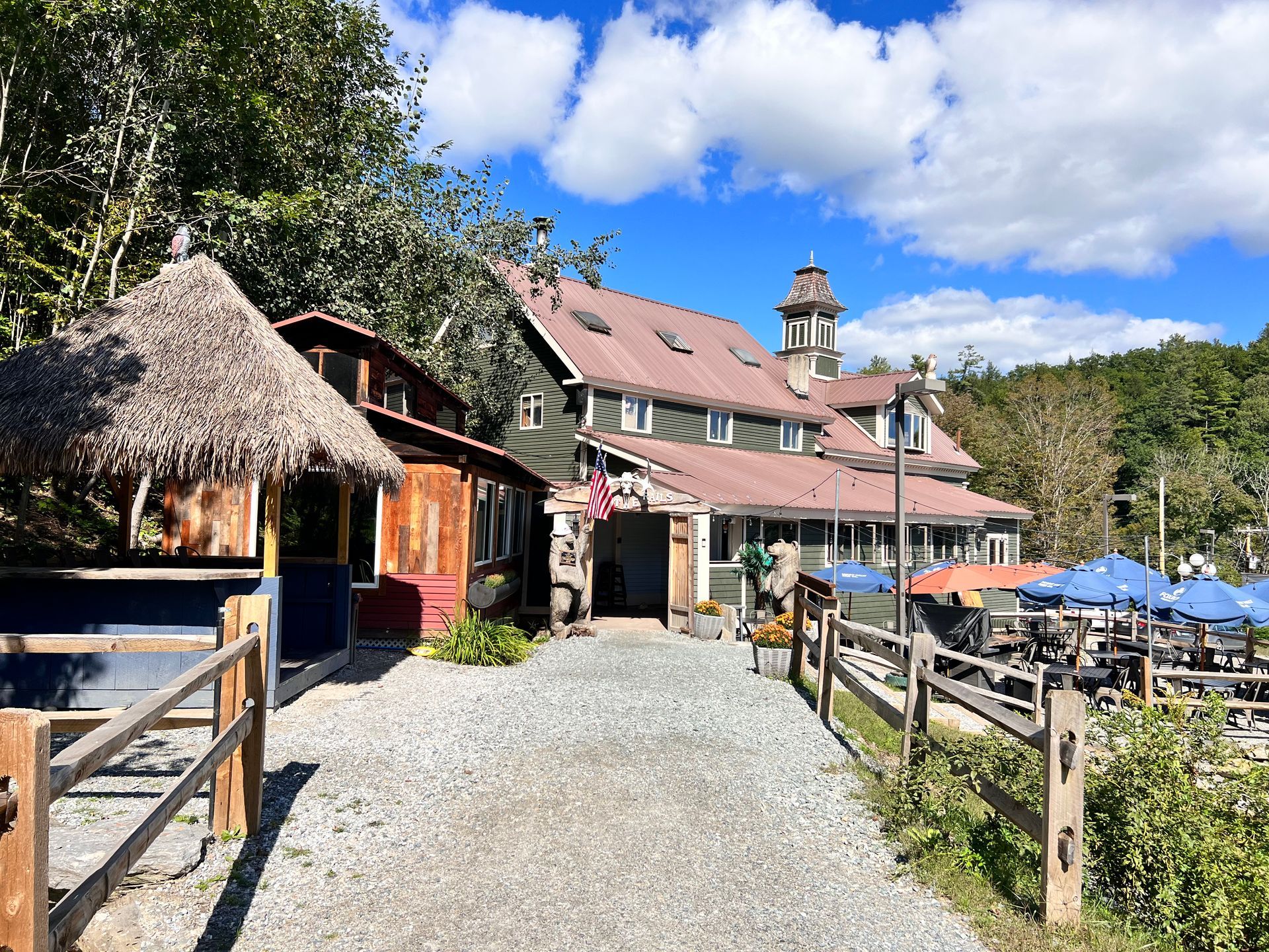 A large building with a thatched roof is surrounded by trees and a gravel path.