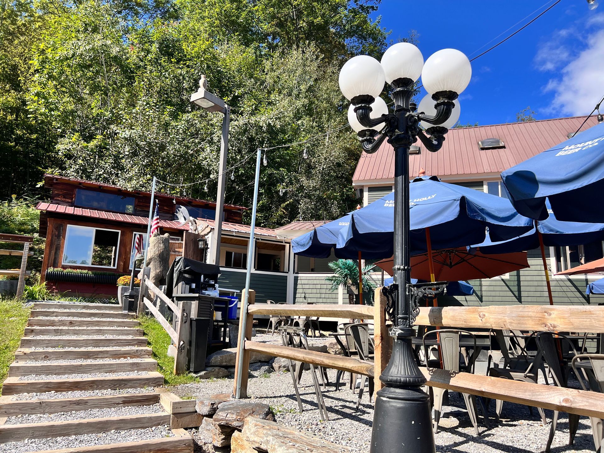 A street light is in front of a restaurant with umbrellas and benches.