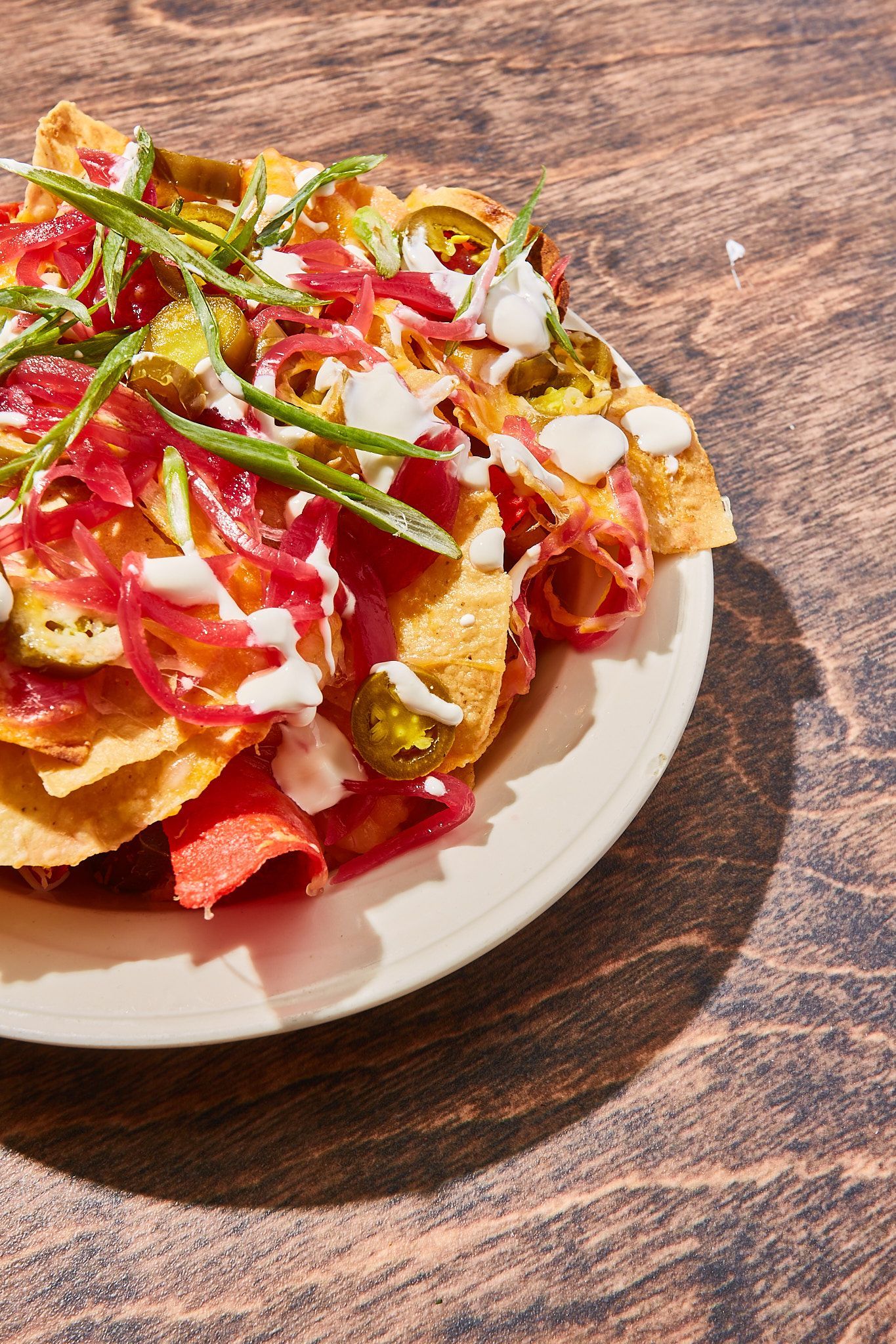A close up of a plate of nachos on a wooden table.