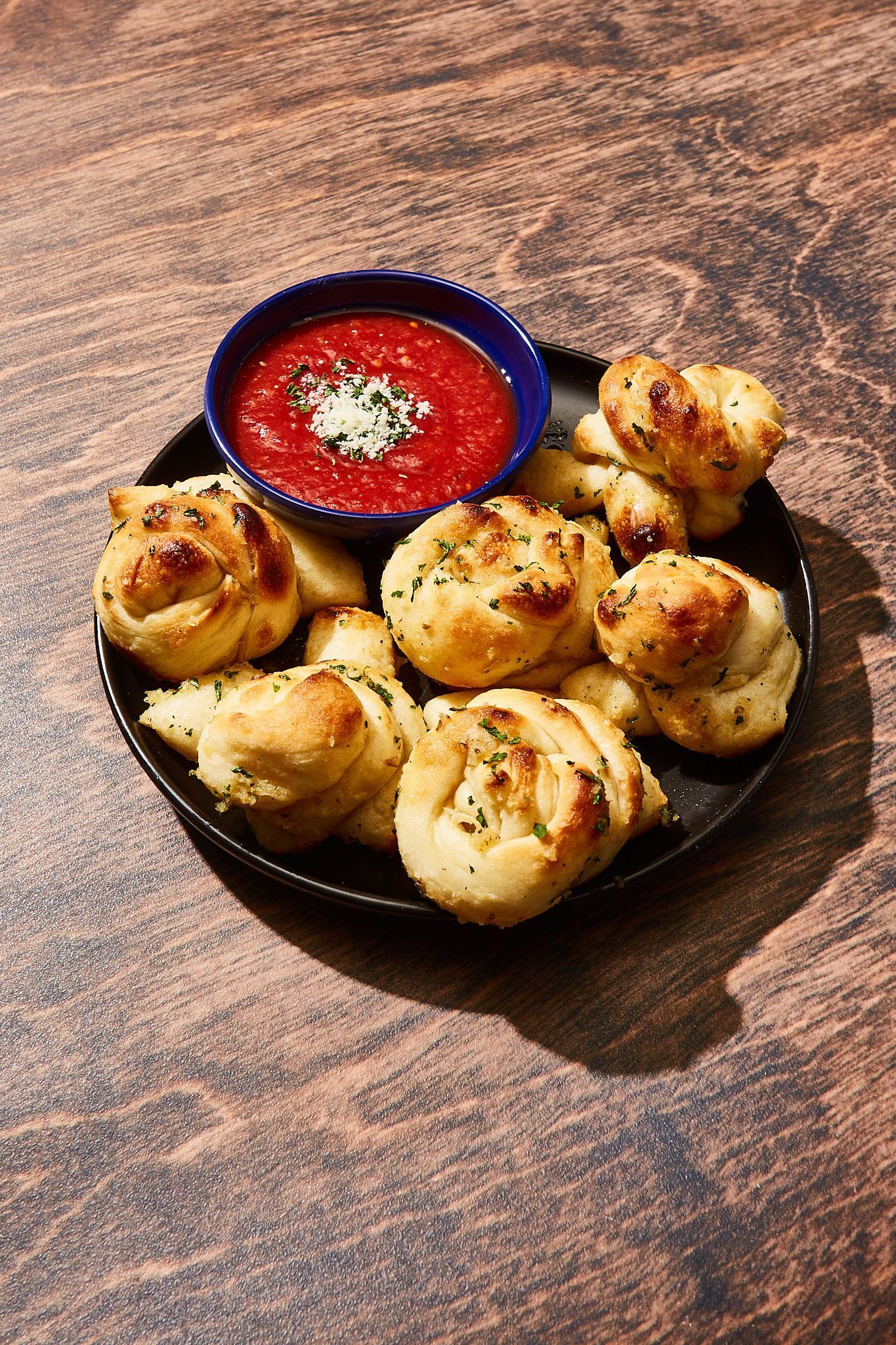 A plate of garlic knots with a bowl of sauce on a table.