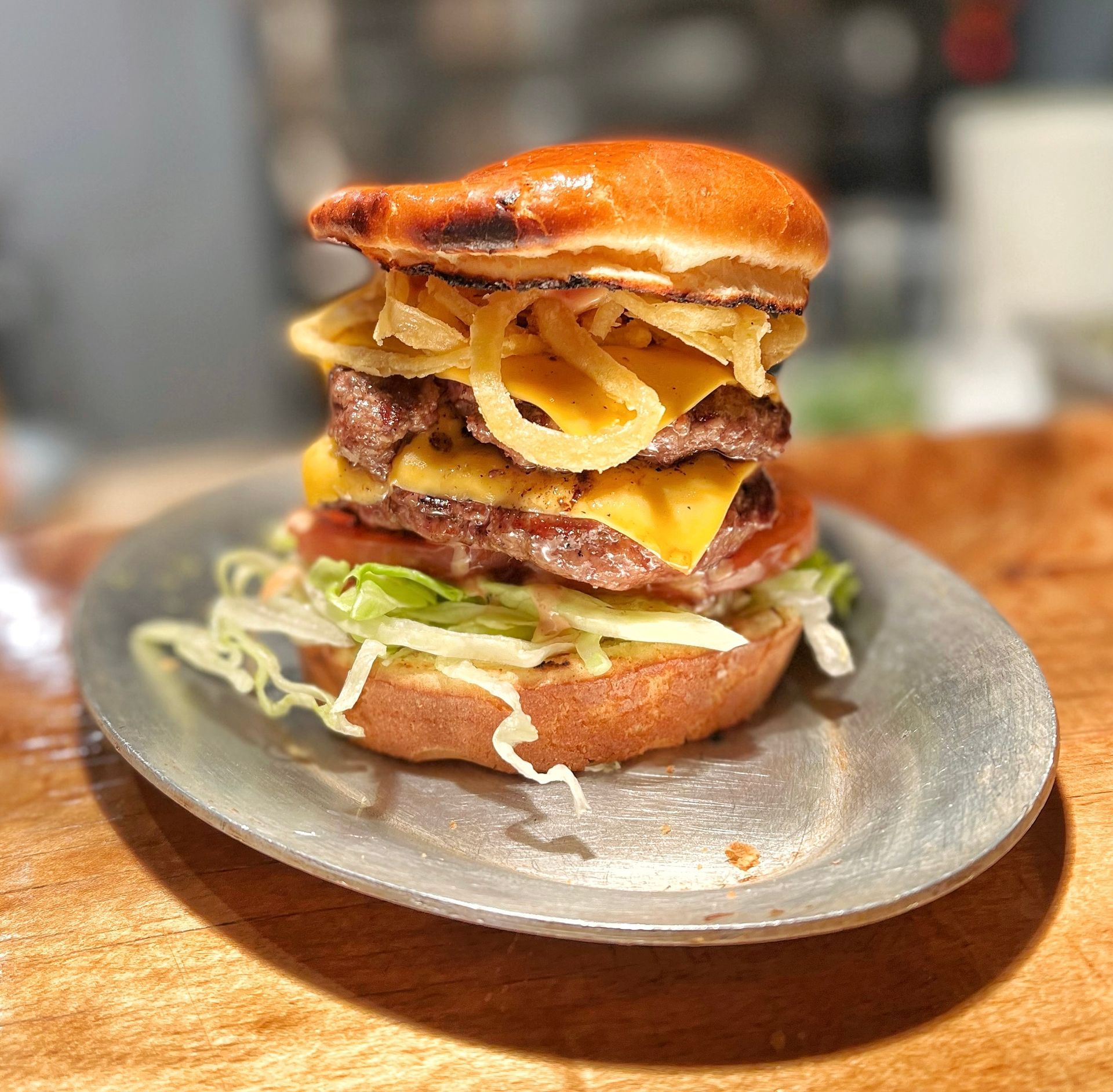 A hamburger is sitting on a metal plate on a wooden table.