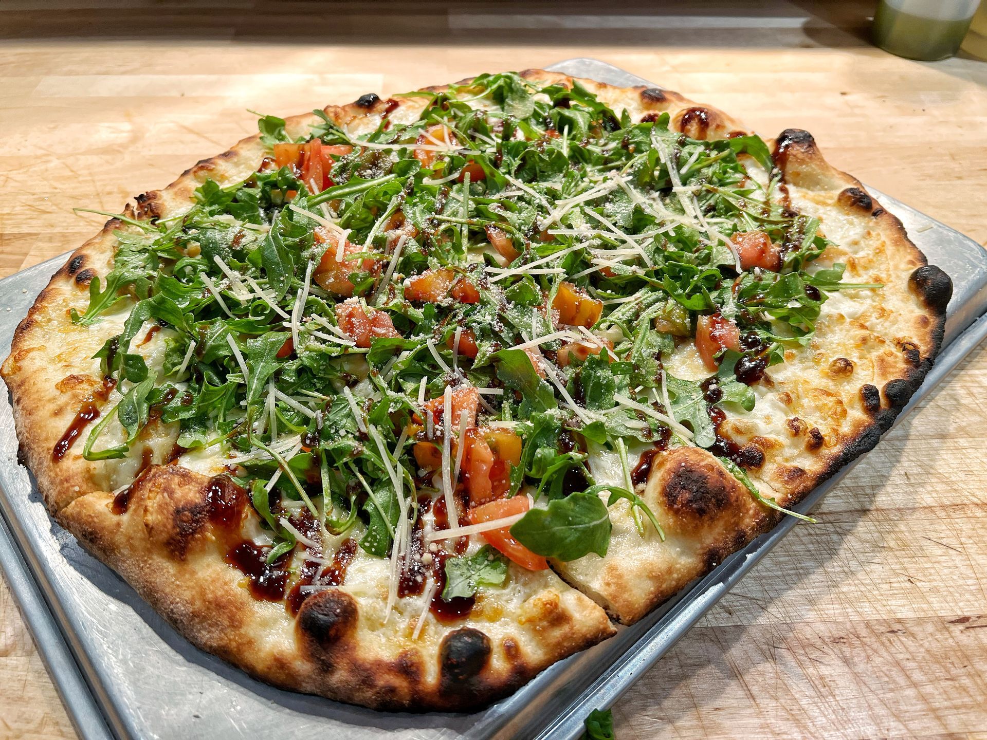 A pizza with a lot of toppings on it is sitting on a metal tray on a wooden table.
