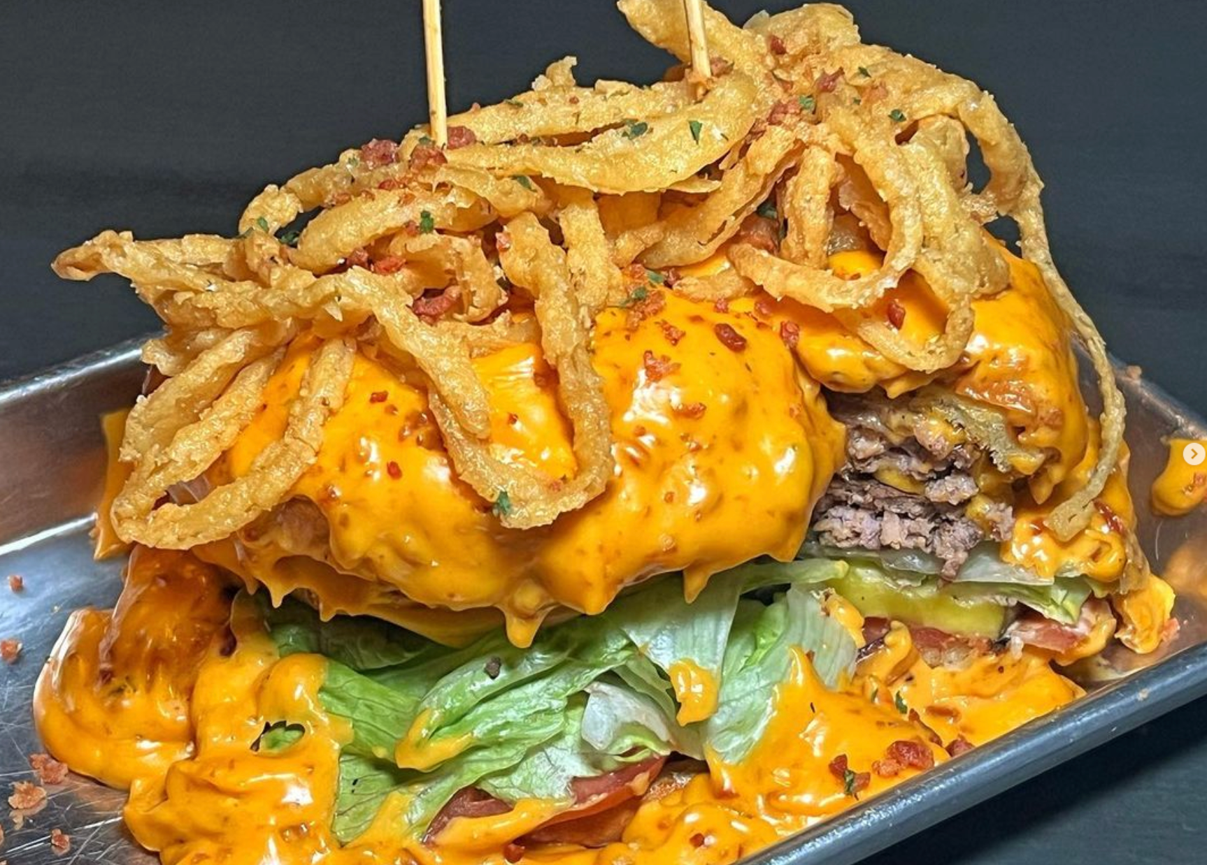A hamburger with cheese lettuce and onion rings on a metal tray
