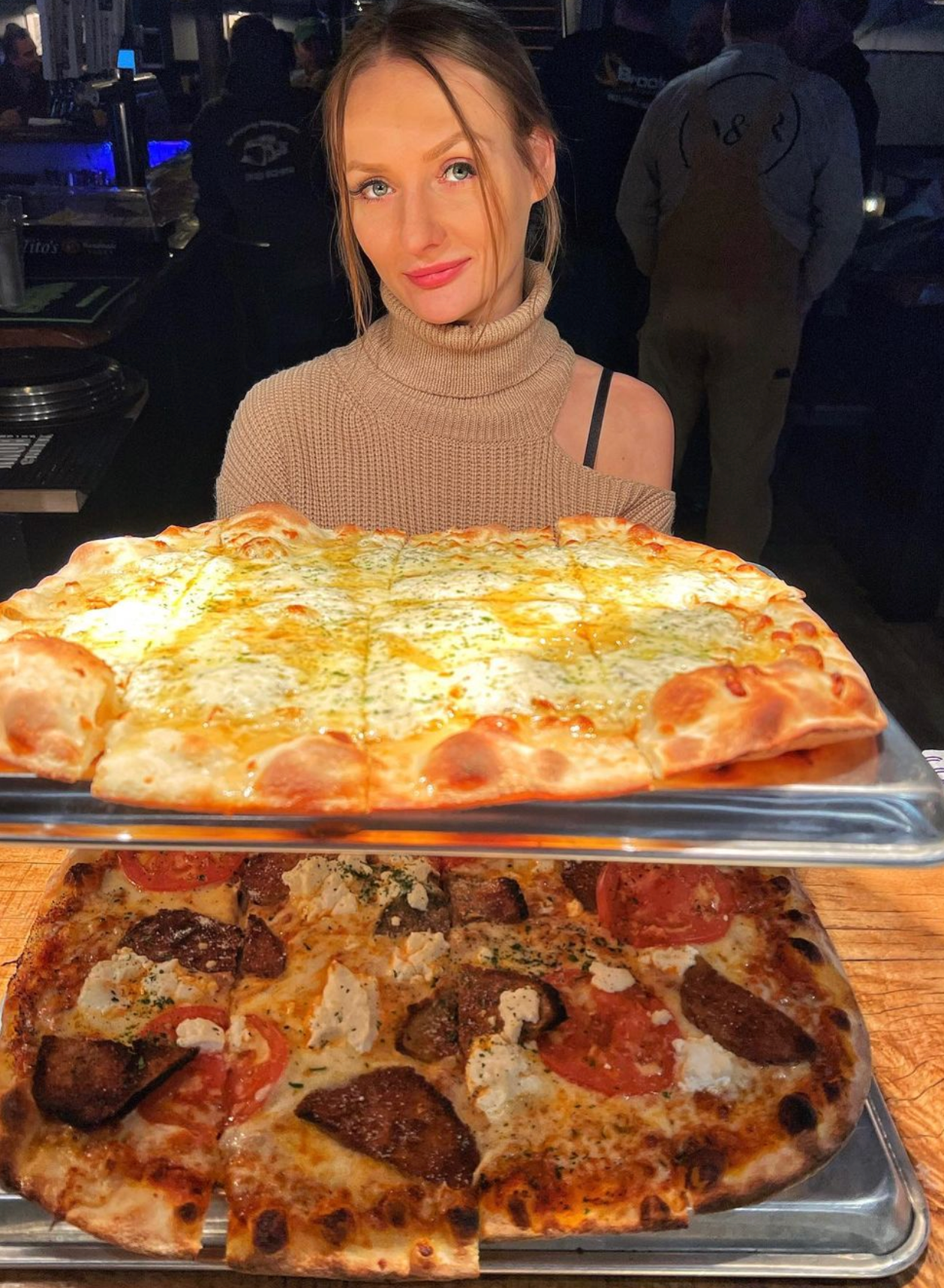 A woman is standing in front of a tray of pizza.