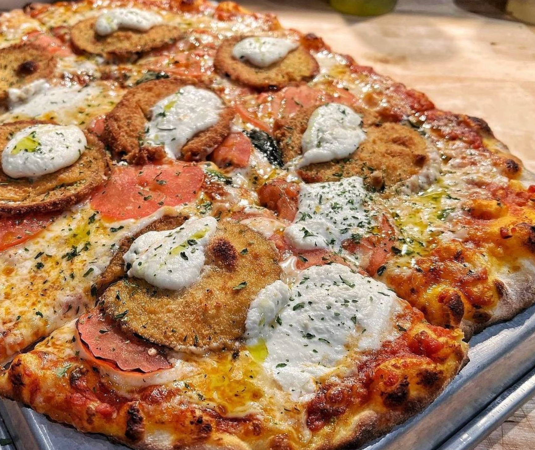 A pizza with a lot of toppings on it is on a pan on a table.