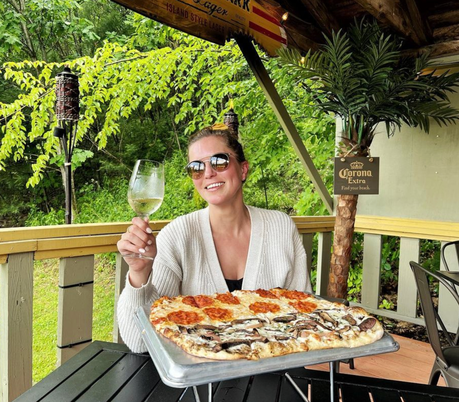 A woman is sitting at a table with a pizza and a glass of wine.