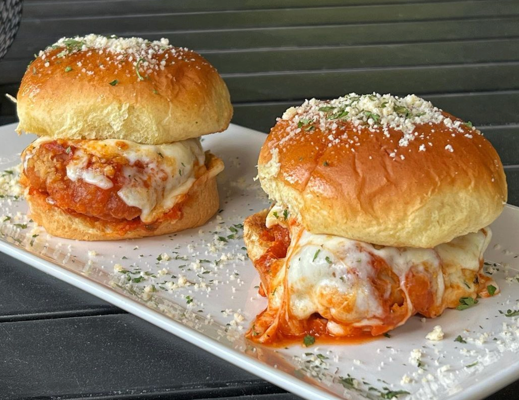 Two meatball sliders on a white plate on a table.