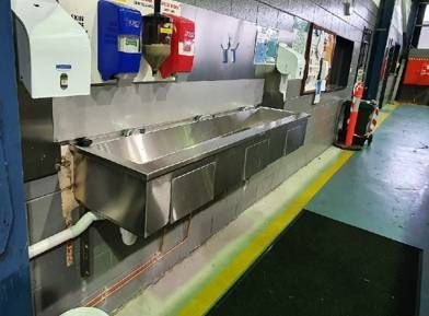 A row of stainless steel sinks are lined up on a wall.